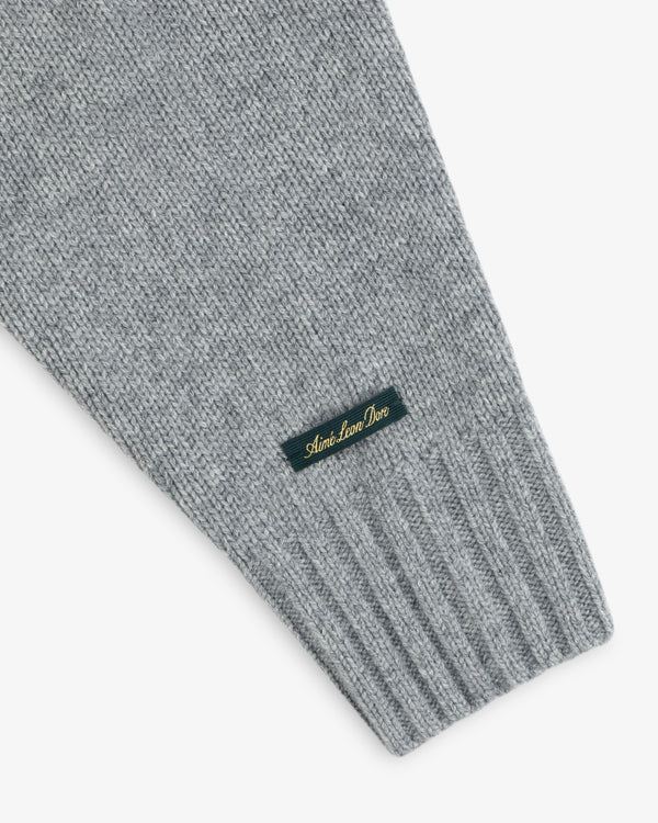 Grey knit sleeve of a Cashmere Crewneck Sweater with a ribbed cuff and a branded label.