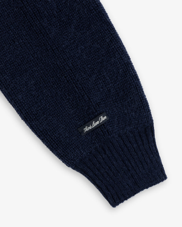 Dark blue ribbed knit sleeve of a Twisted Rib Cardigan with a rectangular brand label sewn near the cuff.