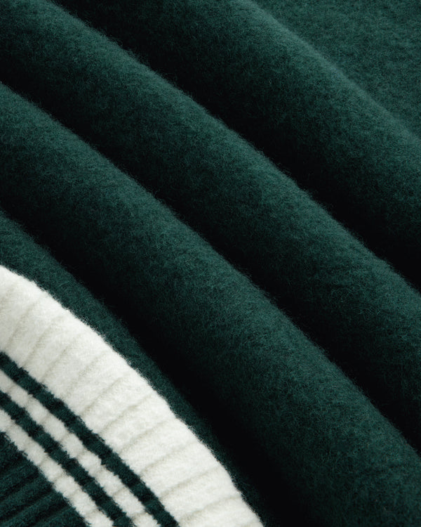 Dark green felted fabric of a Boiled Wool Letterman Sweater folded next to cream-colored ribbed trim with black stripes.