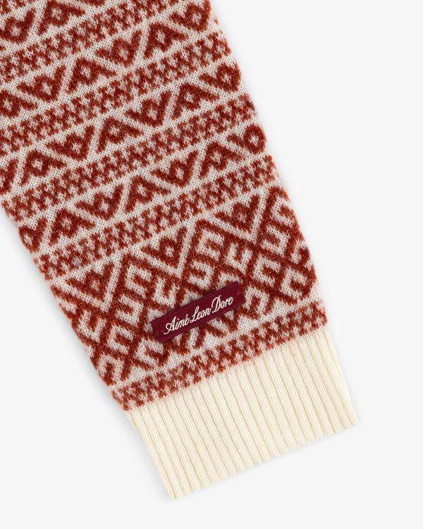 A close-up of a Wool Cashmere Jacquard Cardigan sleeve in a rust and cream geometric pattern with a branded cuff tag.