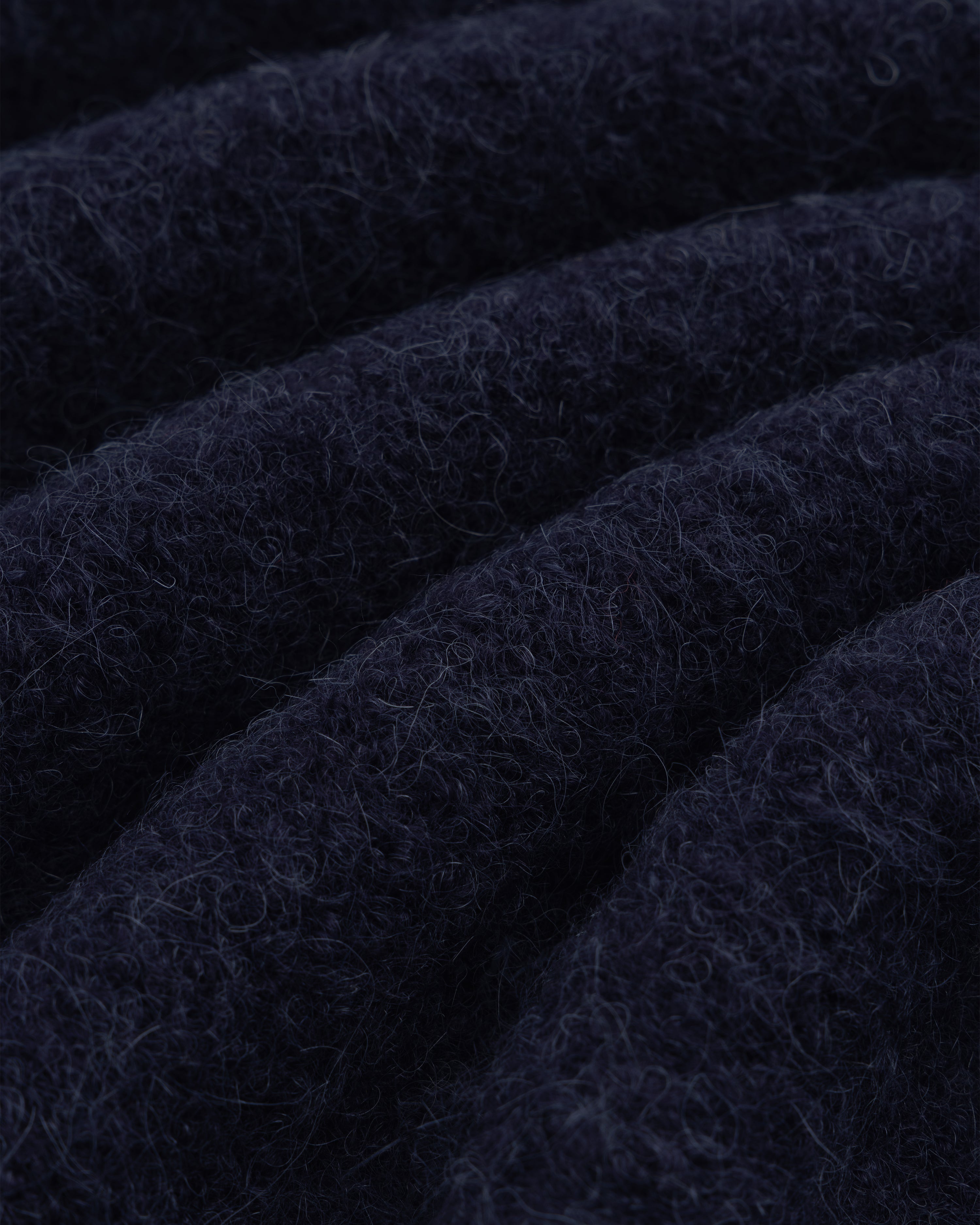 Close-up of dark blue, textured alpaca wool from our Quarter Zip Sweater, showing visible fibers and soft folds.