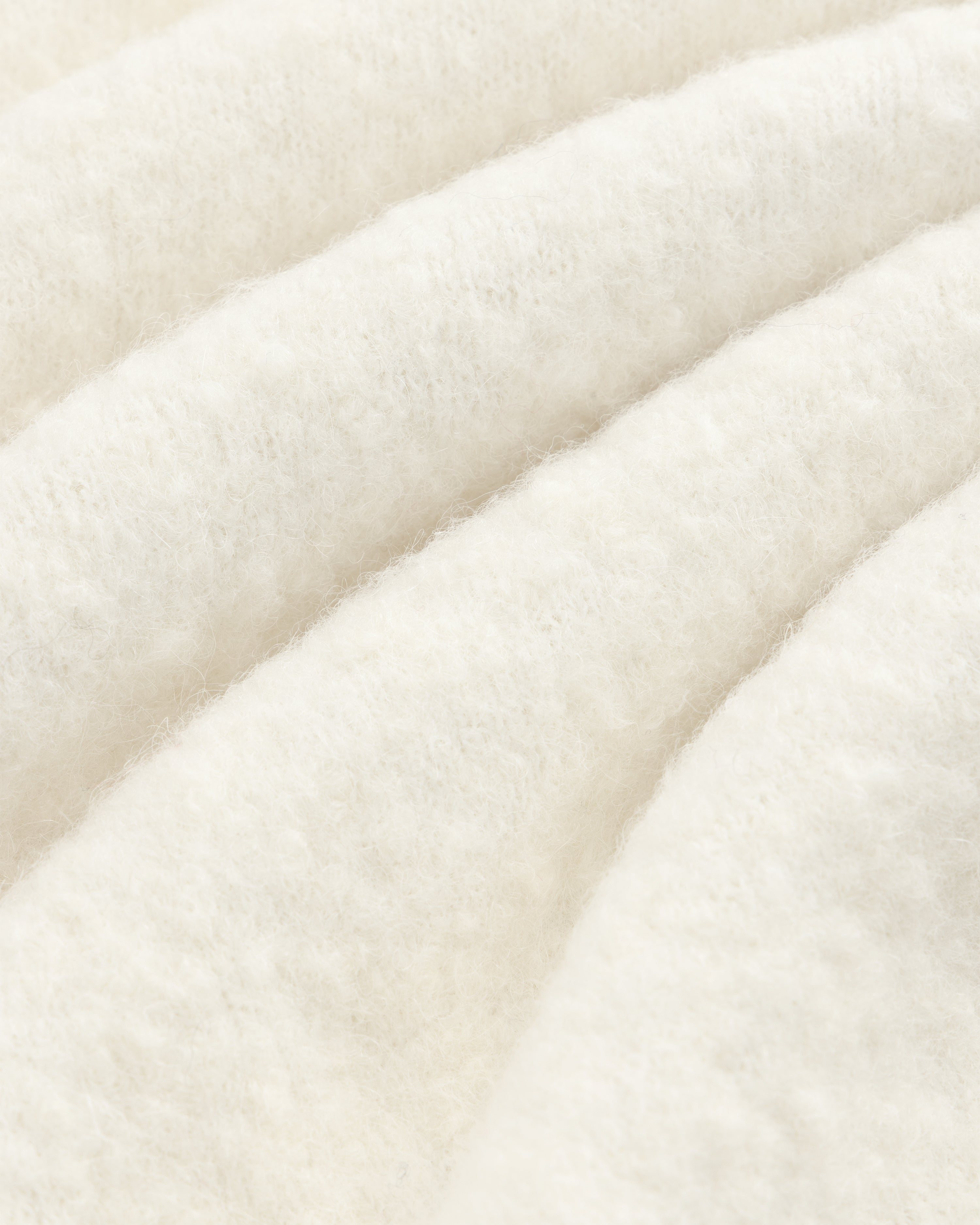 Close-up of the Alpaca Wool Quarter Zip Sweater, showcasing its white, fluffy texture and cozy, wavy folds.