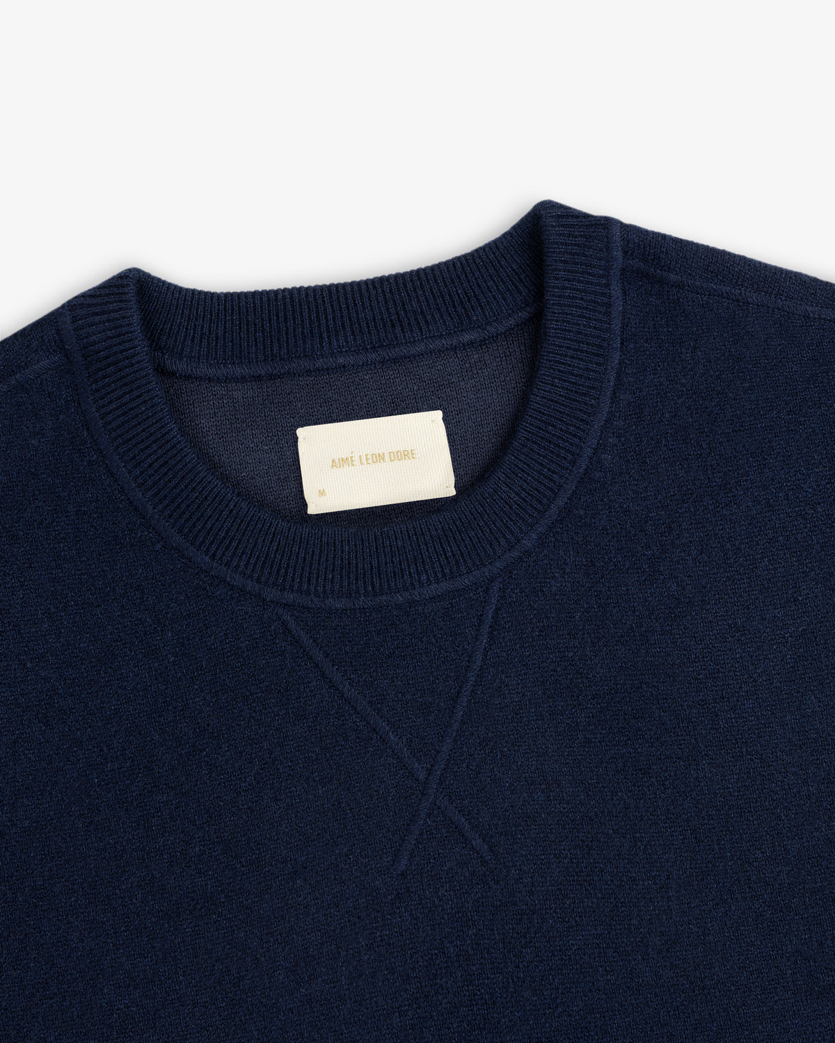 Close-up of a navy Pavilion Cashmere Crewneck Sweatshirt with ribbed collar and a beige AIME LEON DORE label.