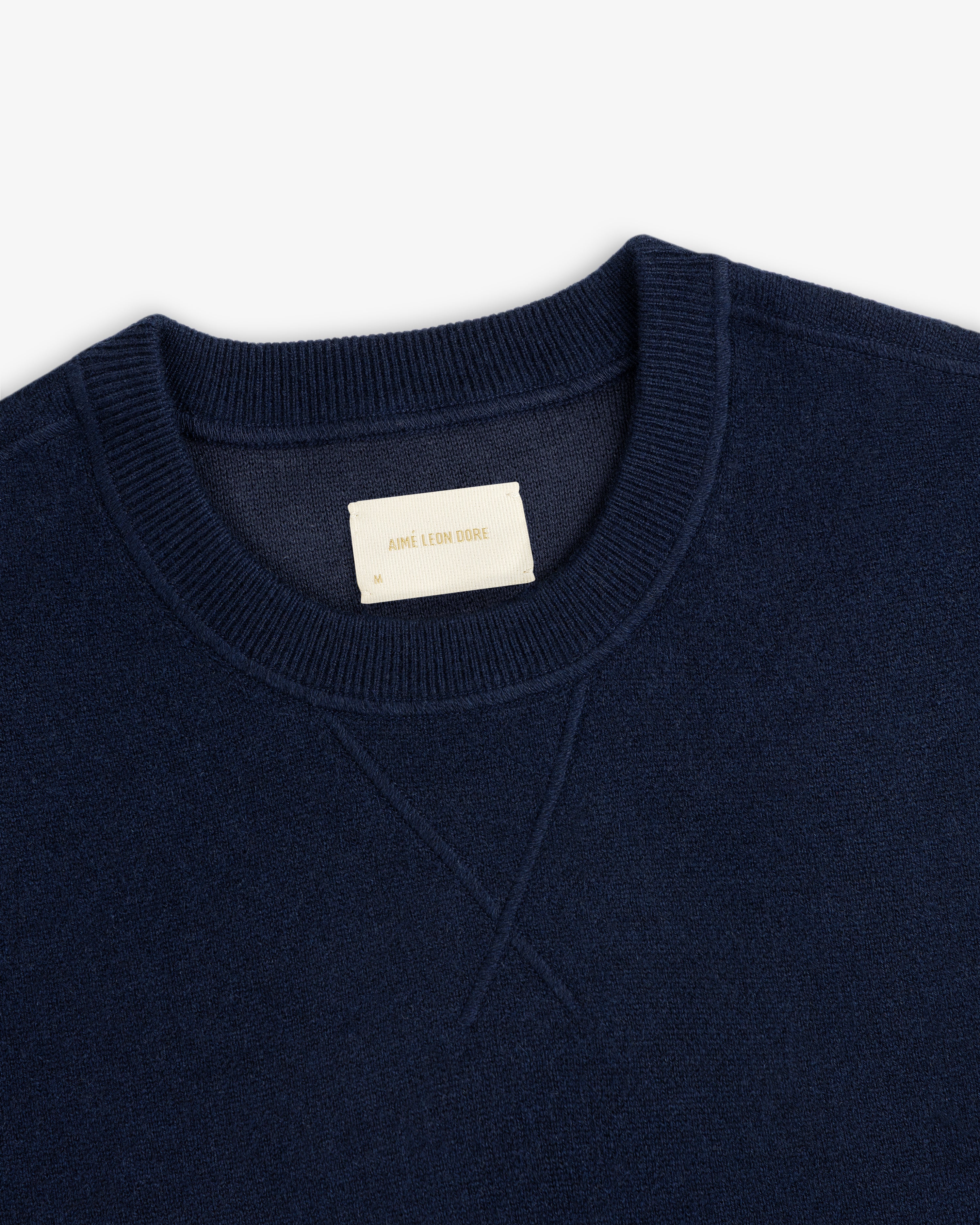 Close-up of a navy Pavilion Cashmere Crewneck Sweatshirt with ribbed collar and a beige AIME LEON DORE label.