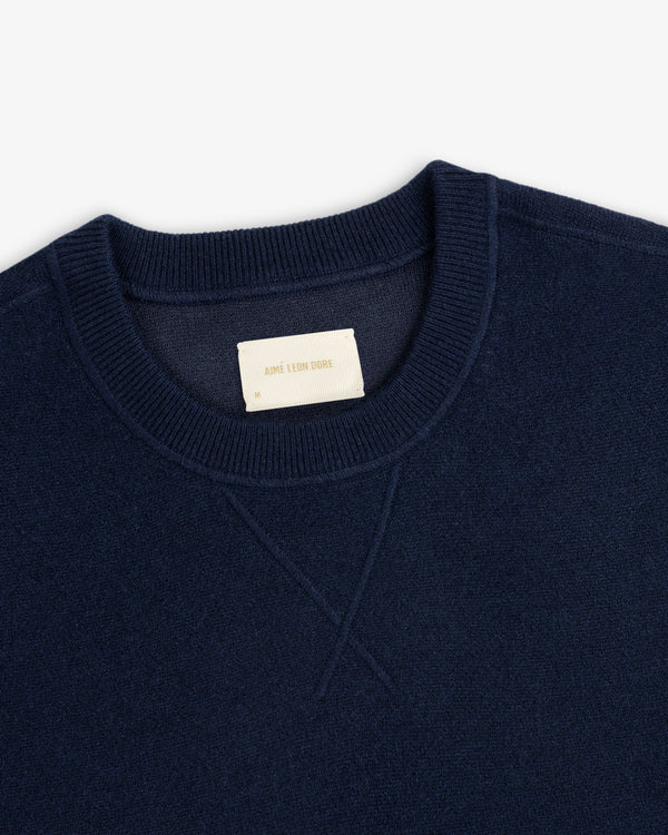 Close-up of a navy Pavilion Cashmere Crewneck Sweatshirt with ribbed collar and a beige AIME LEON DORE label.