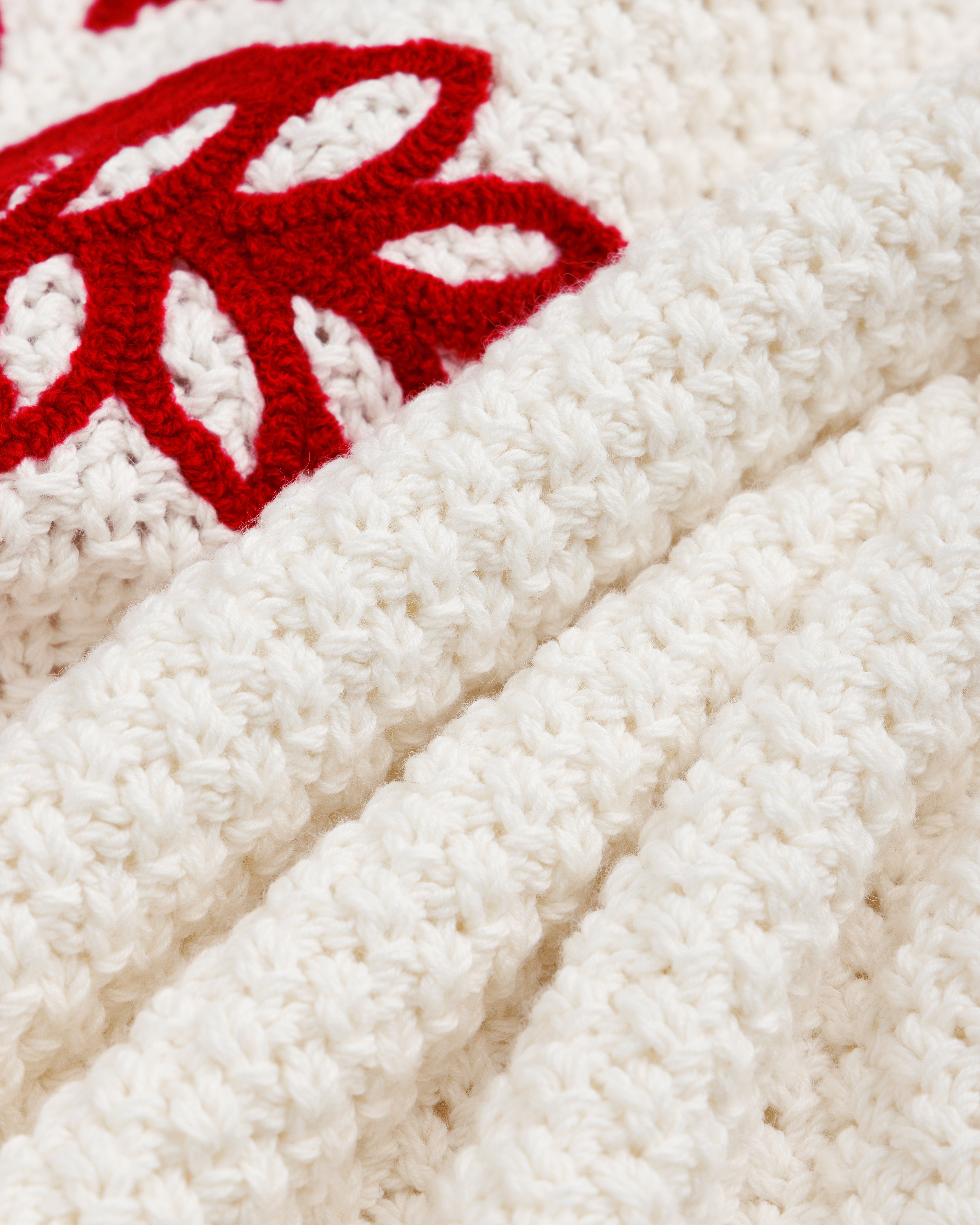 Cream-colored ALD / Olympiacos F.C. Knit V-Neck Sweater with a red embroidered floral or emblem design.