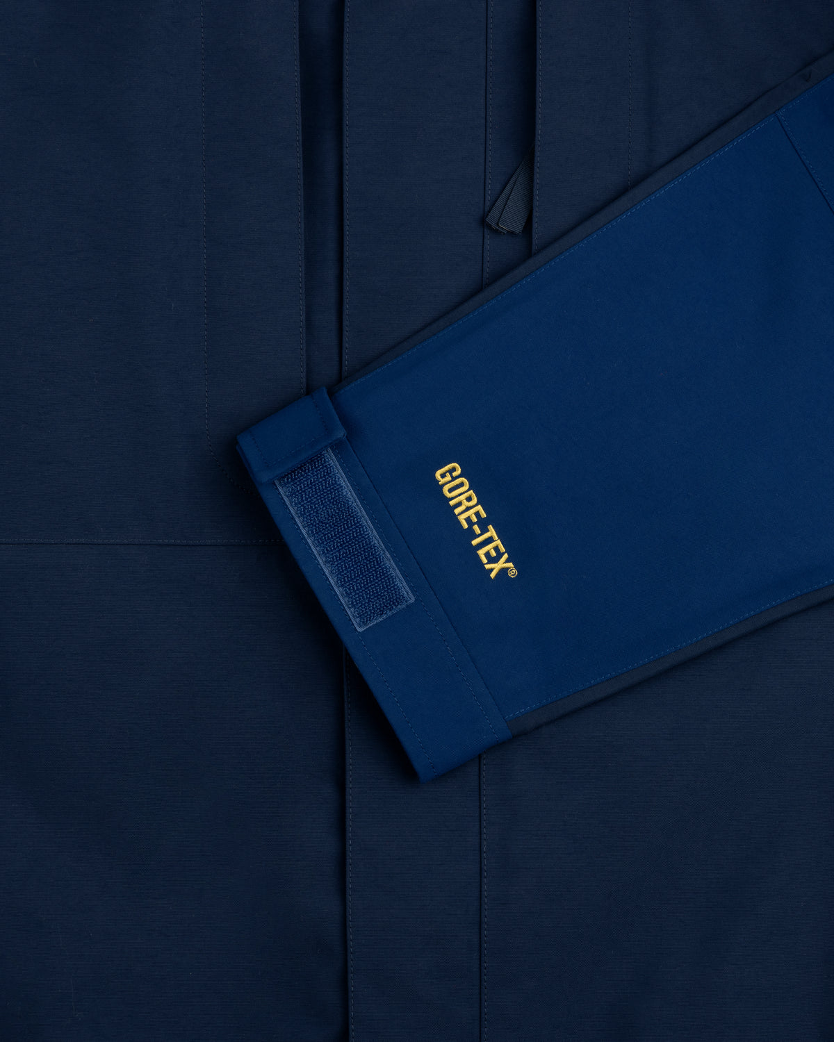 Close-up of ALD/The North Face GORE-TEX 2000 Mountain Jacket sleeve with Velcro cuff on matching blue background.