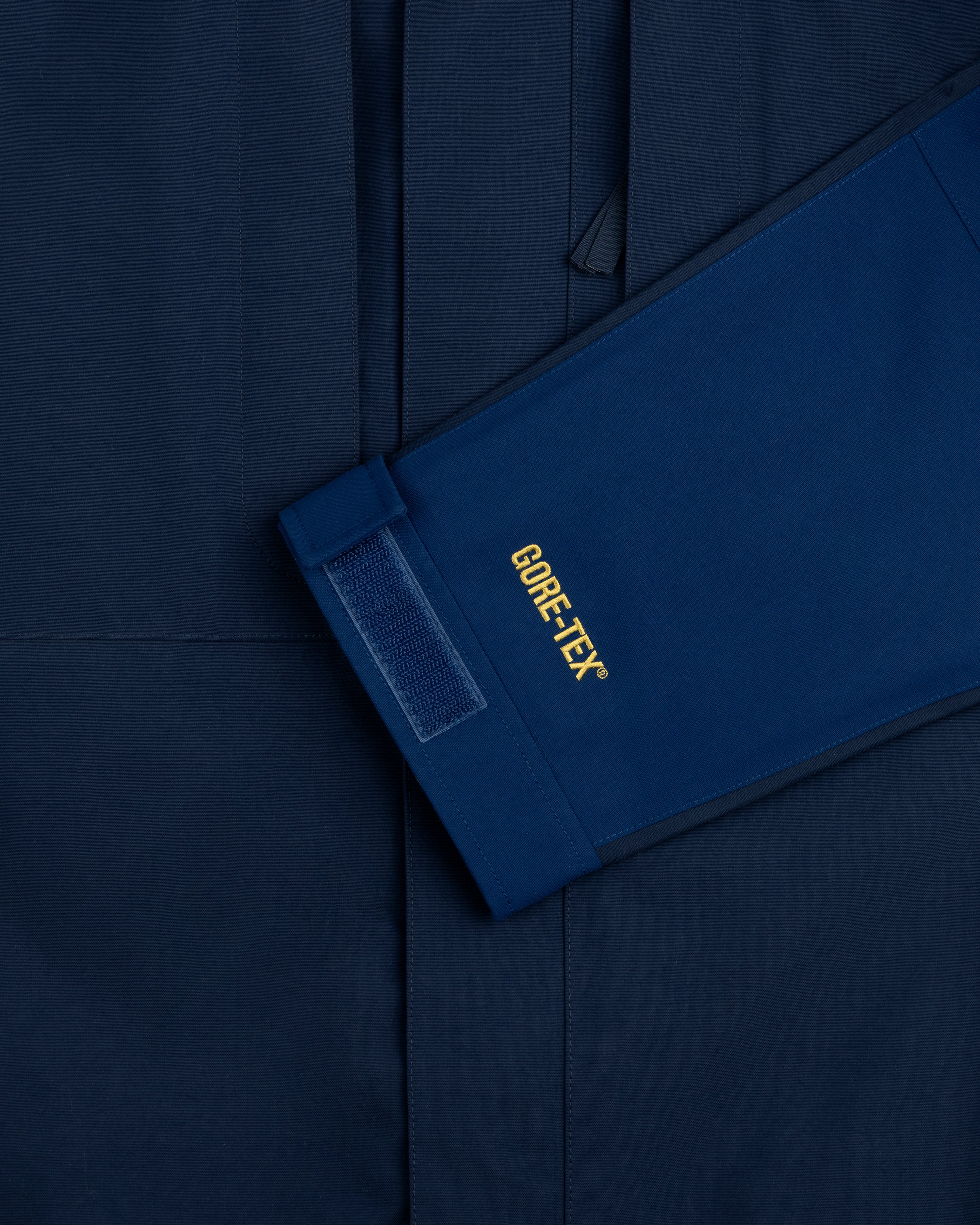 Close-up of ALD/The North Face GORE-TEX 2000 Mountain Jacket sleeve with Velcro cuff on matching blue background.