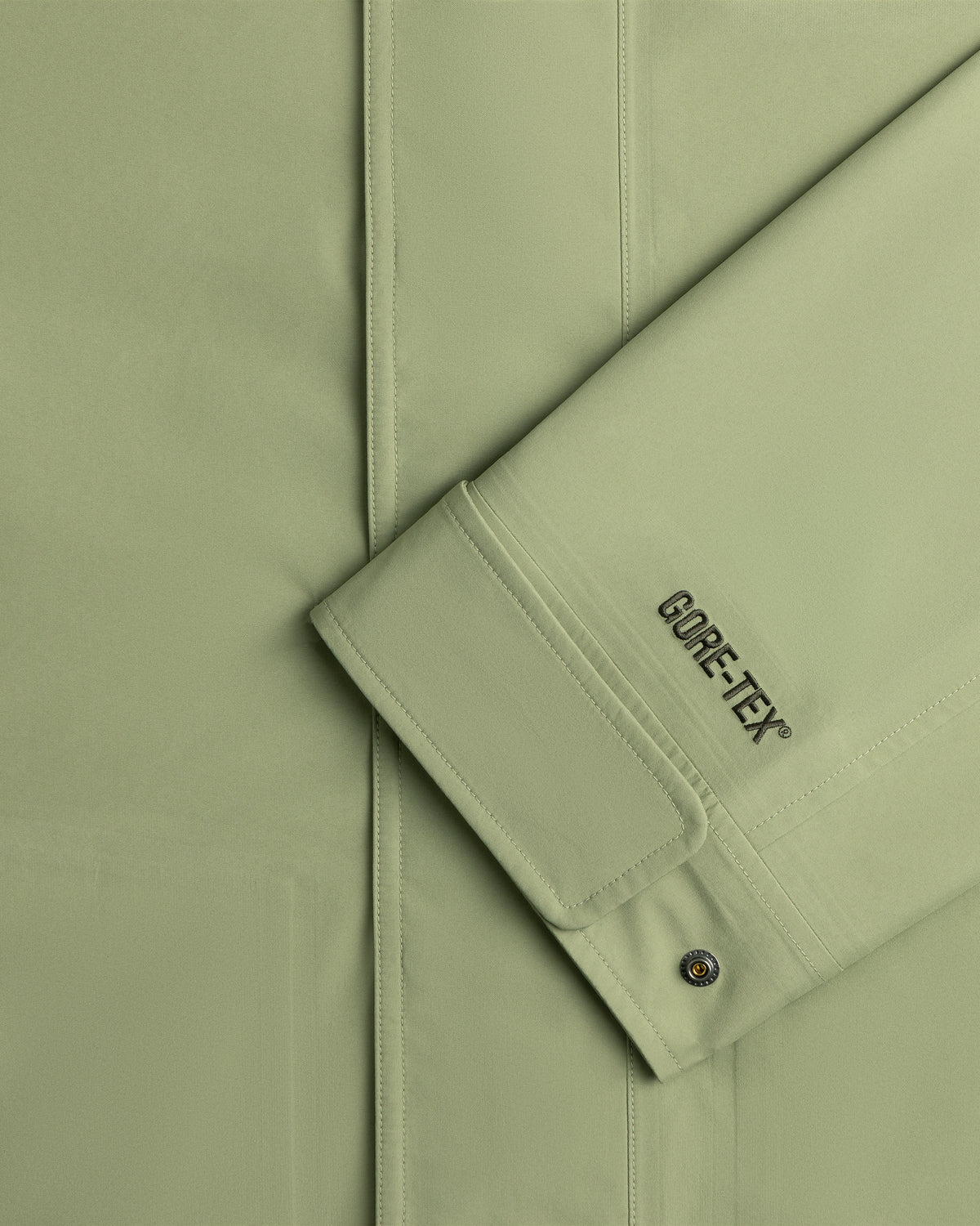 Close-up of a light green ALD/The North Face GORE-TEX Trench Coat sleeve with seam and metal snap button on cuff.