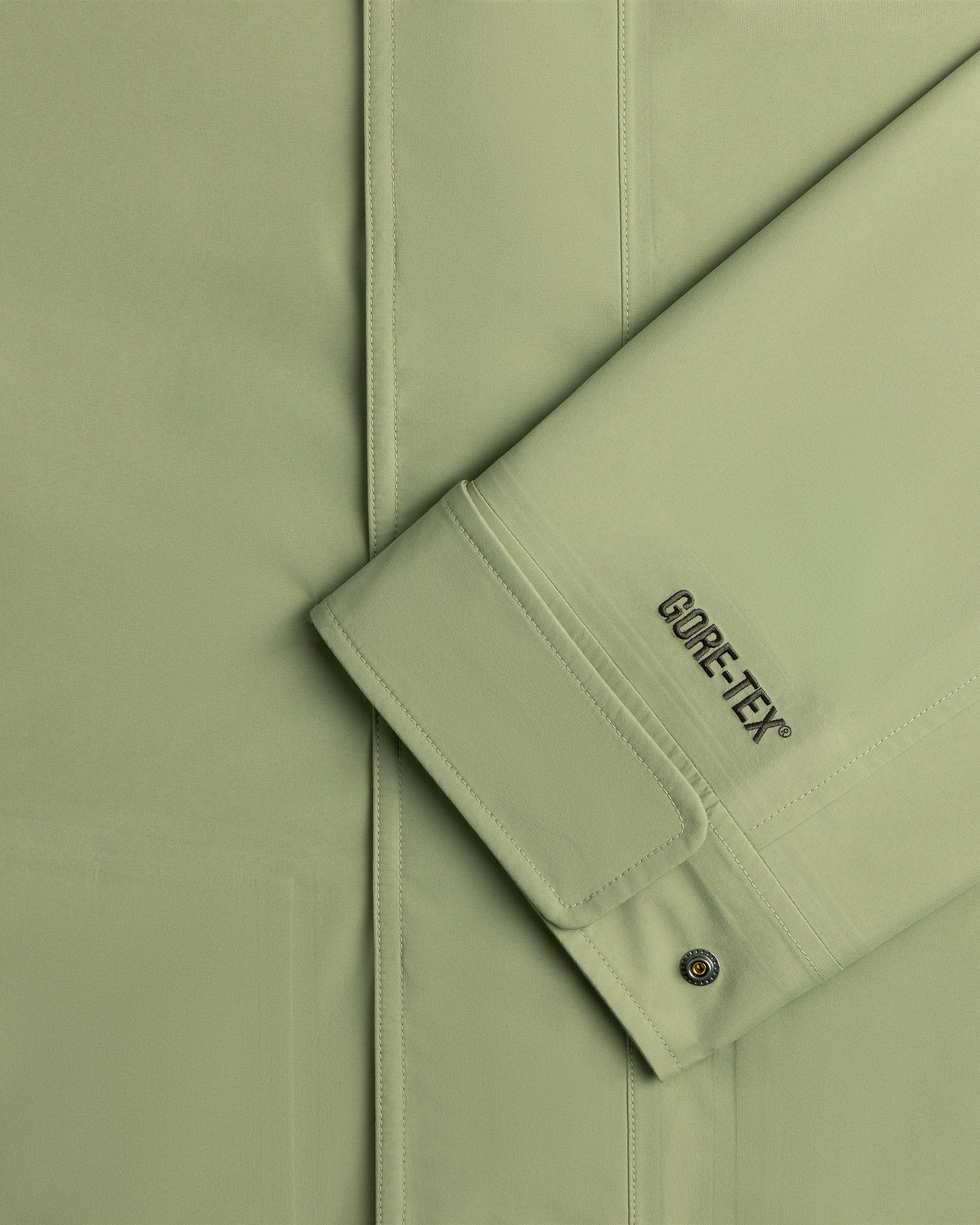 Close-up of a light green ALD/The North Face GORE-TEX Trench Coat sleeve with seam and metal snap button on cuff.