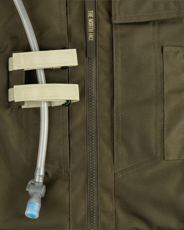 Close-up of an olive green ALD / The North Face Ballistic Tech Vest with hydration tube secured by two beige straps.