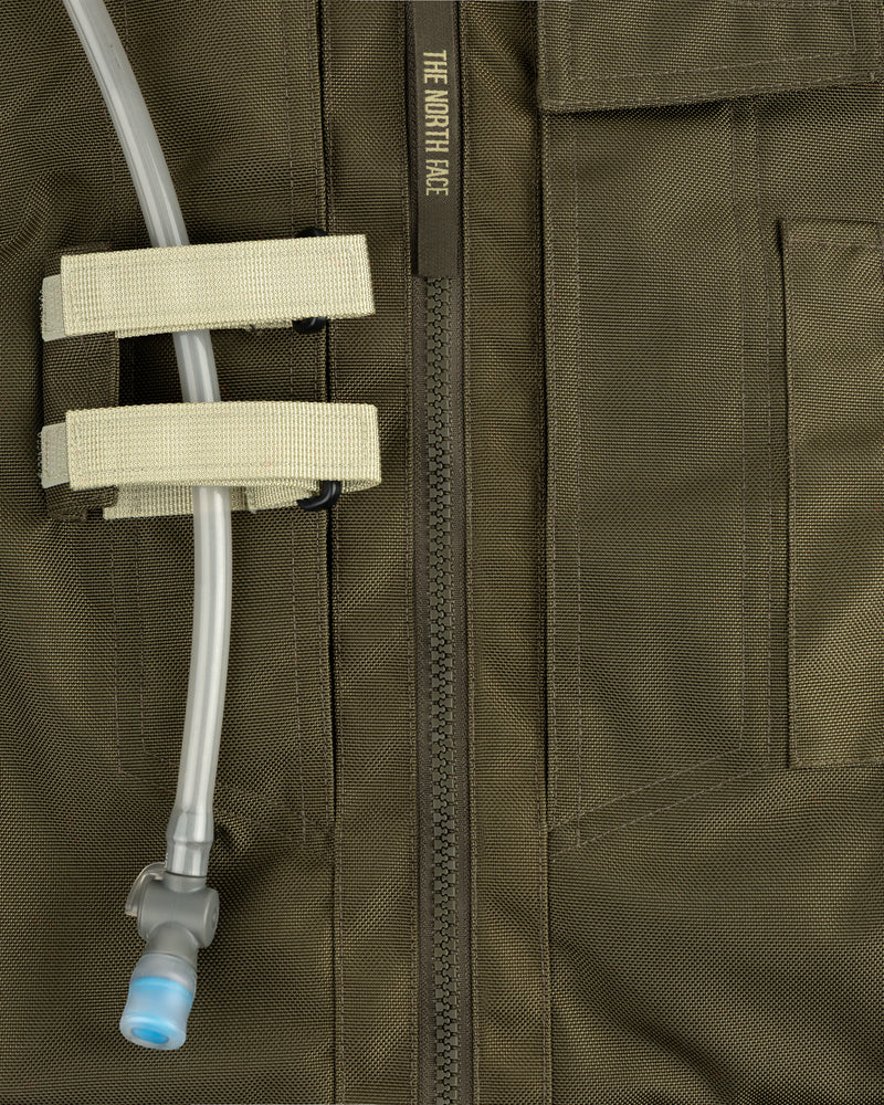 Close-up of an olive green ALD / The North Face Ballistic Tech Vest with hydration tube secured by two beige straps.