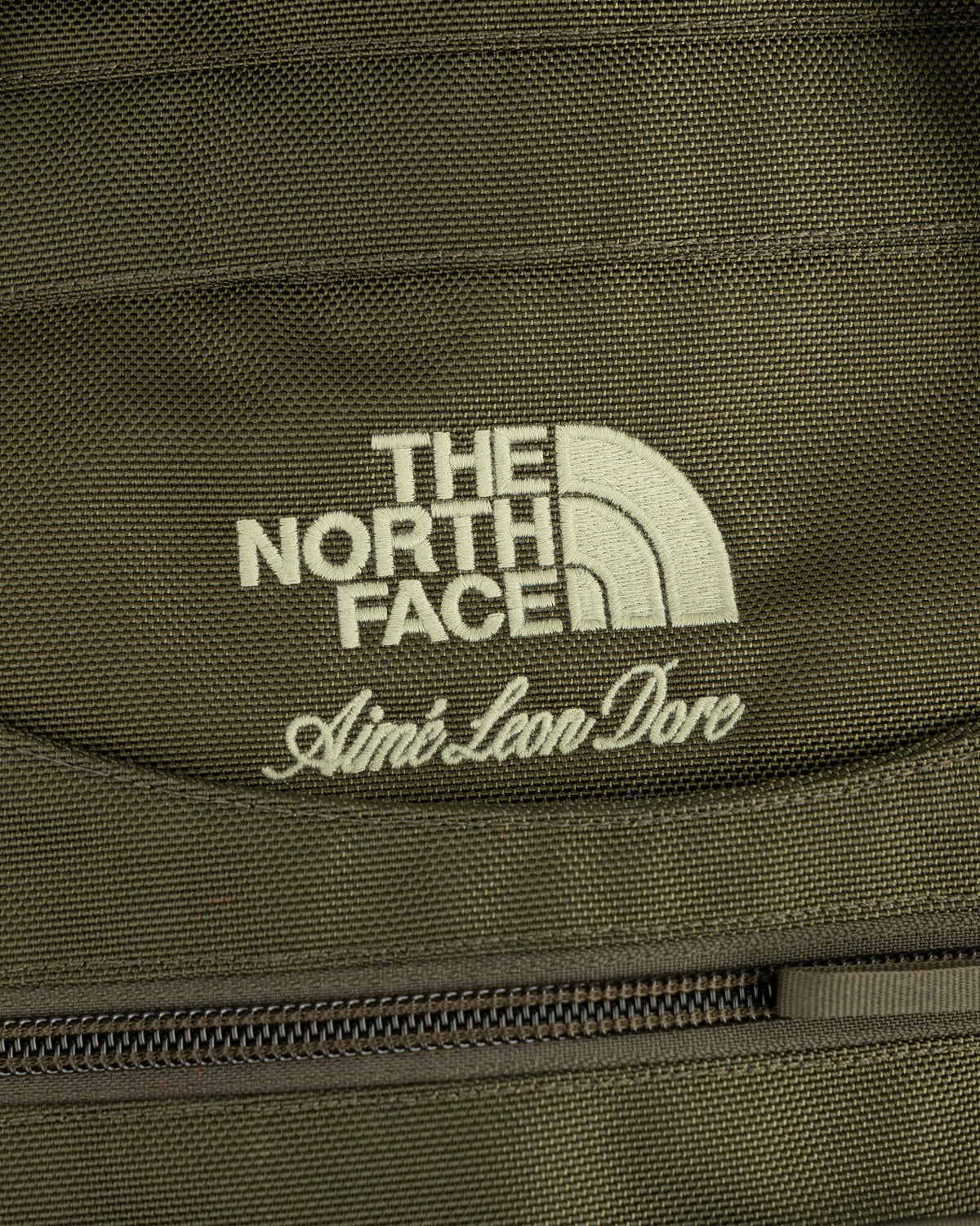 Close-up of olive ALD / The North Face Ballistic Tech Vest with logos above a zipper.