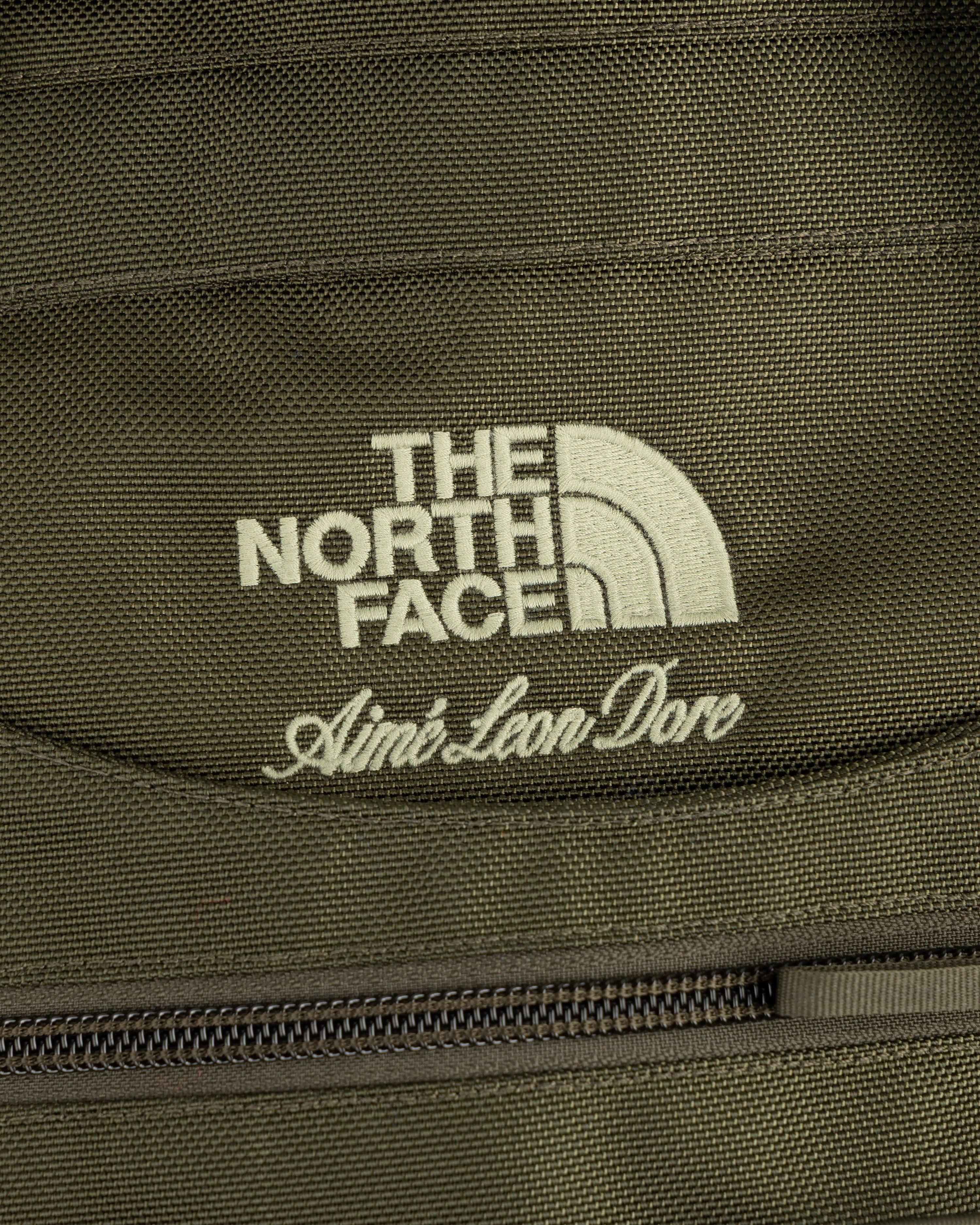 Close-up of olive ALD / The North Face Ballistic Tech Vest with logos above a zipper.