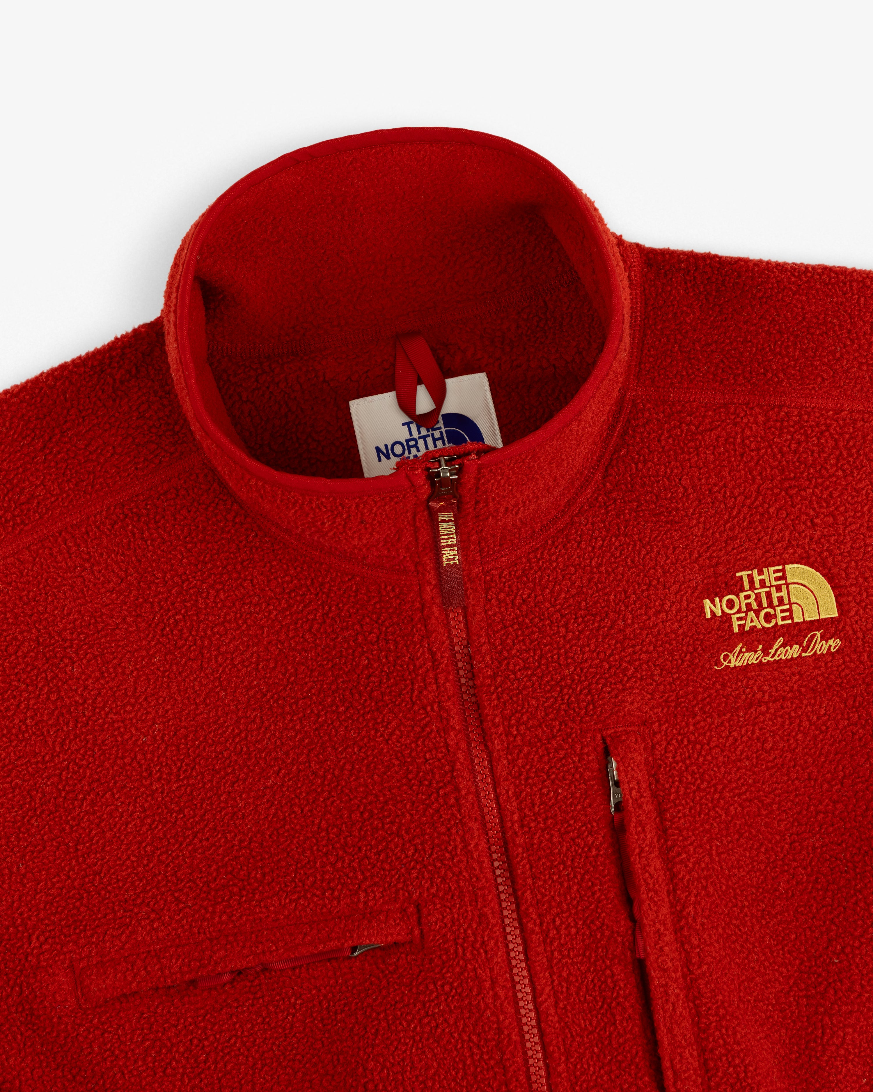 Close-up of a red ALD / The North Face ’95 Denali Half-Zip Fleece Pullover with yellow embroidery and chest zip.