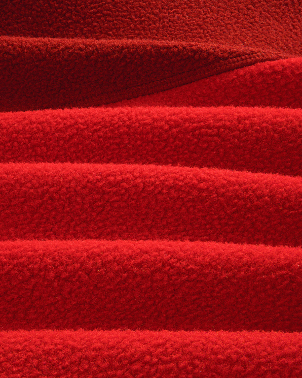 Close-up of ALD/The North Face ’95 Denali Half-Zip Fleece, showing red fabric’s soft, textured ridges and shadows.