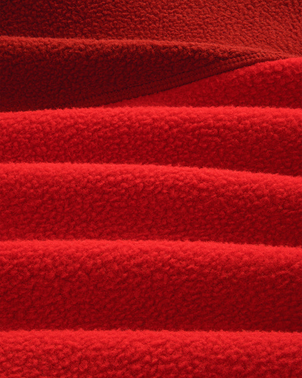 Close-up of ALD/The North Face ’95 Denali Half-Zip Fleece, showing red fabric’s soft, textured ridges and shadows.