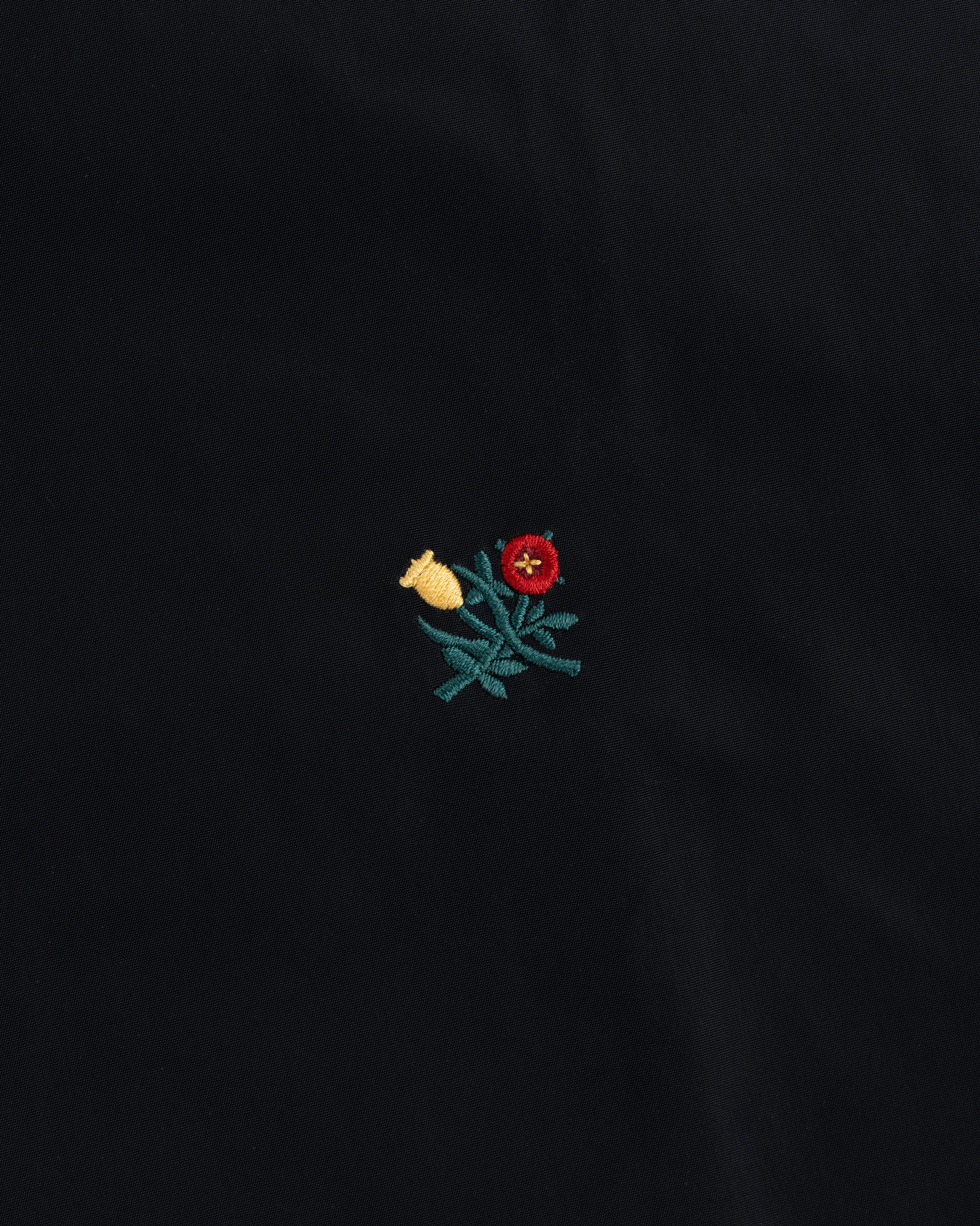 Small red and yellow floral embroidery with green leaves on the black Crest Nylon Windbreaker.