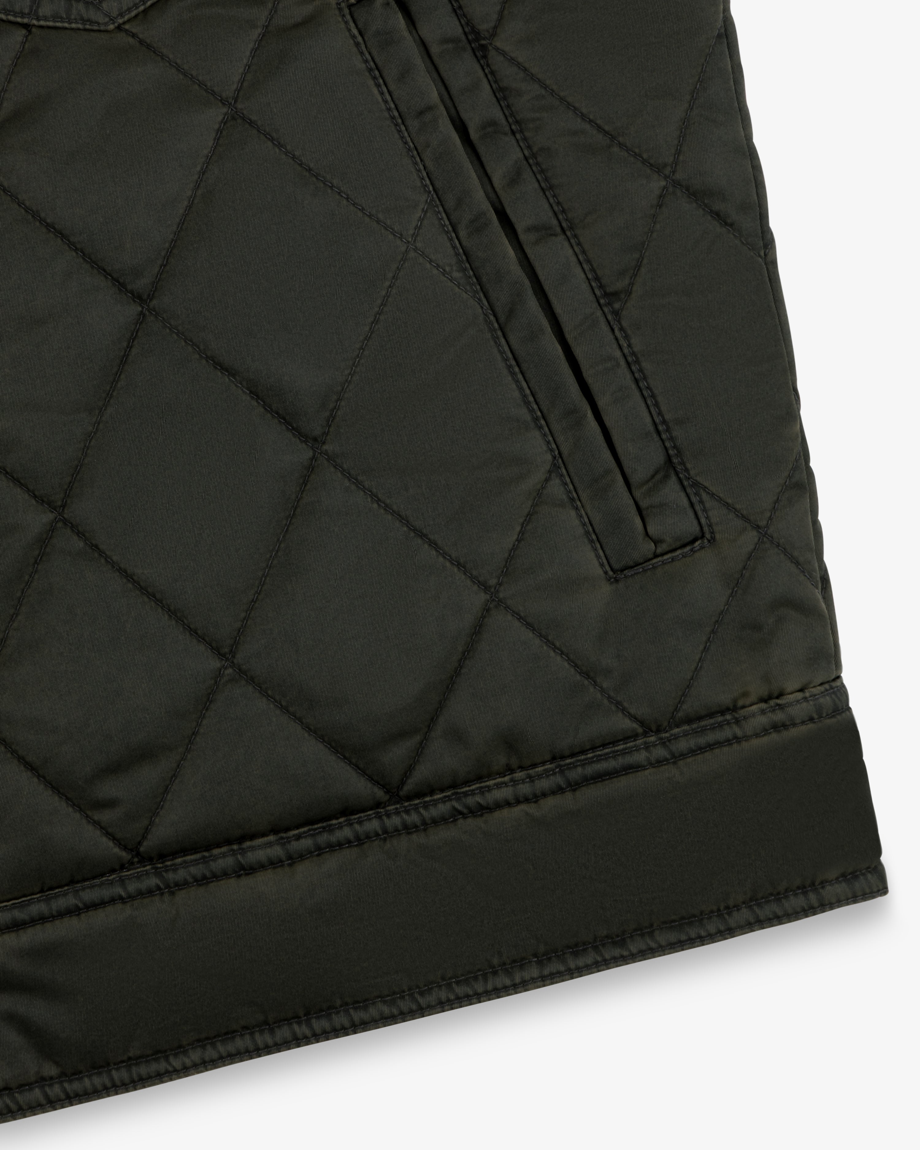 Close-up of a dark olive Quilted Trucker Jacket featuring a side pocket and a wide hem band.