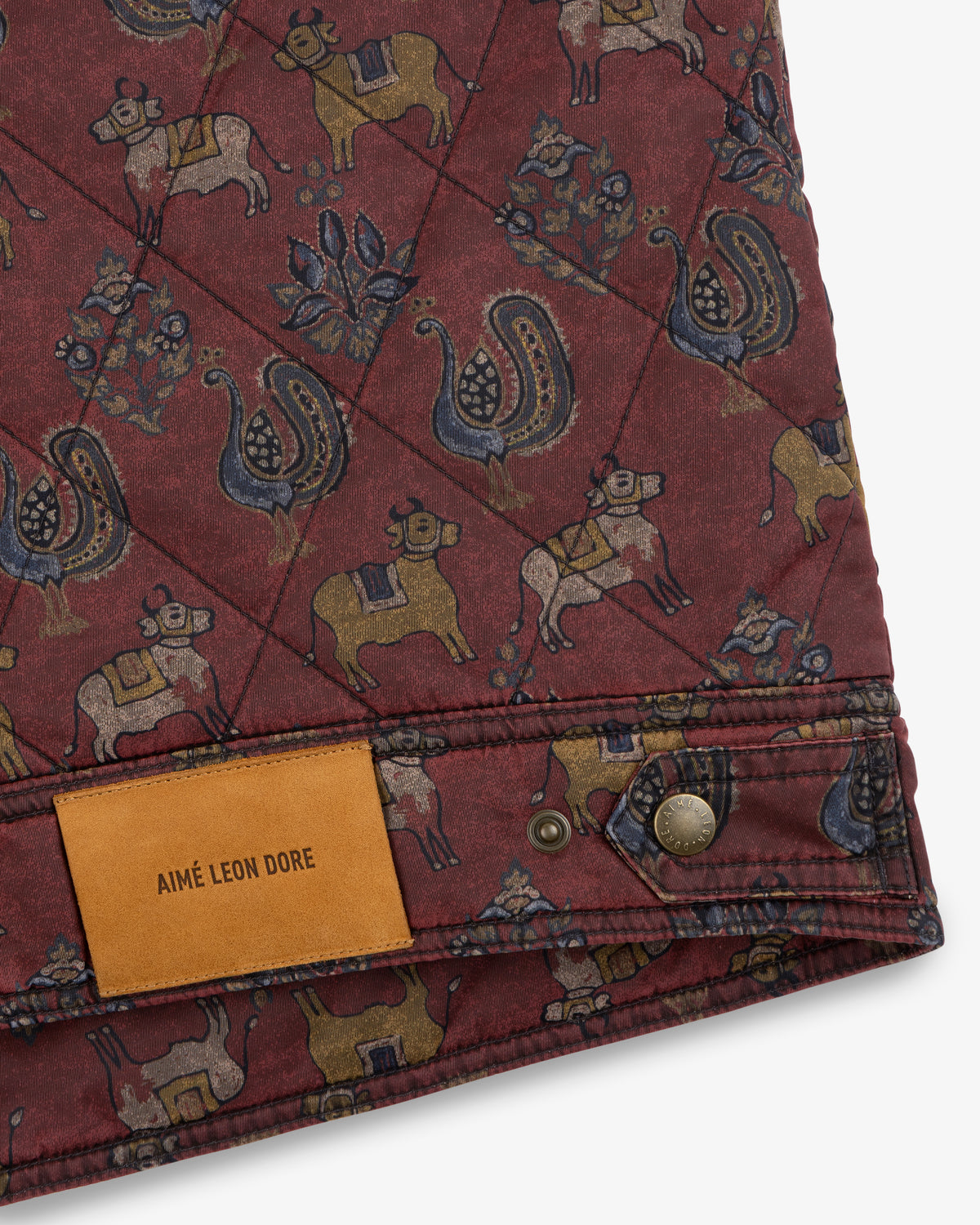 Quilted Trucker Jacket in maroon with a cattle and bird print and a tan leather brand label at the hem.