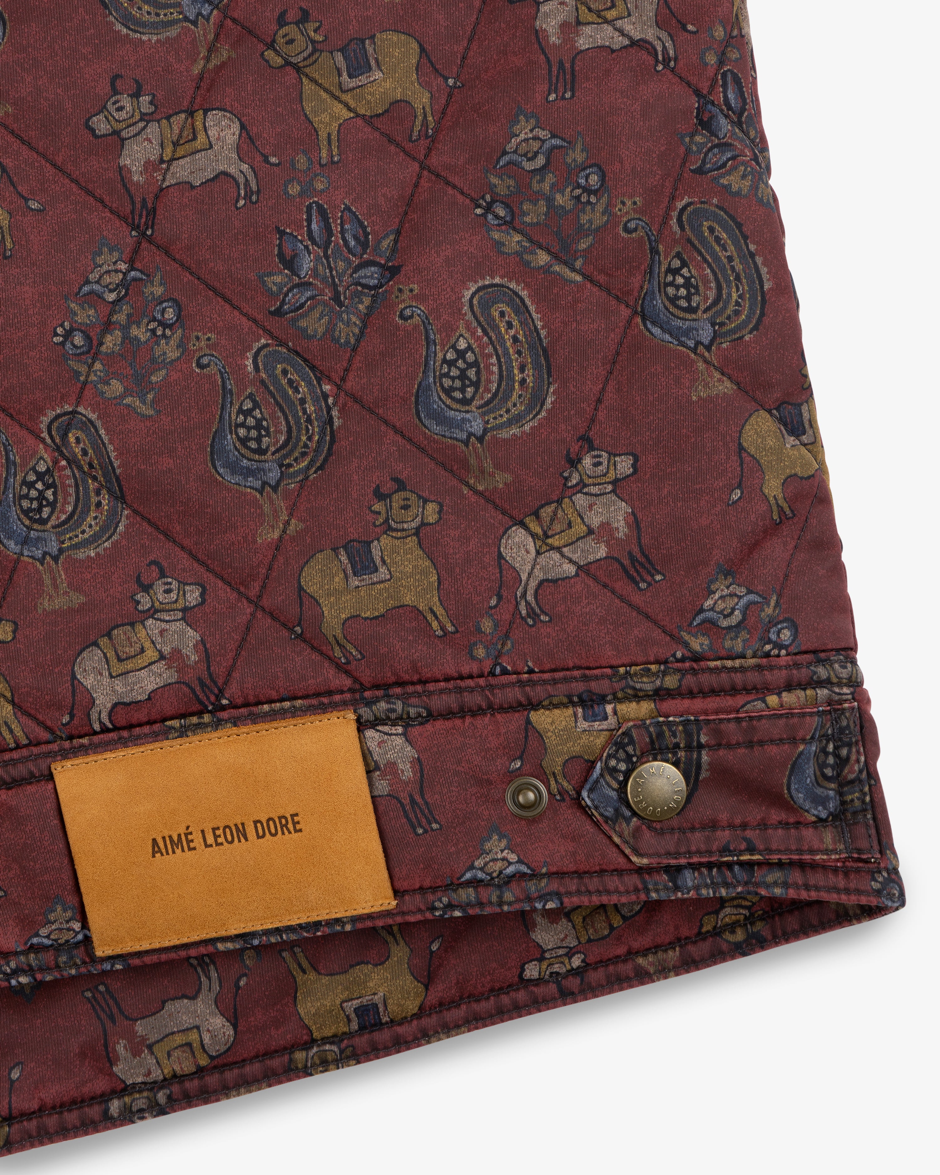 Quilted Trucker Jacket in maroon with a cattle and bird print and a tan leather brand label at the hem.