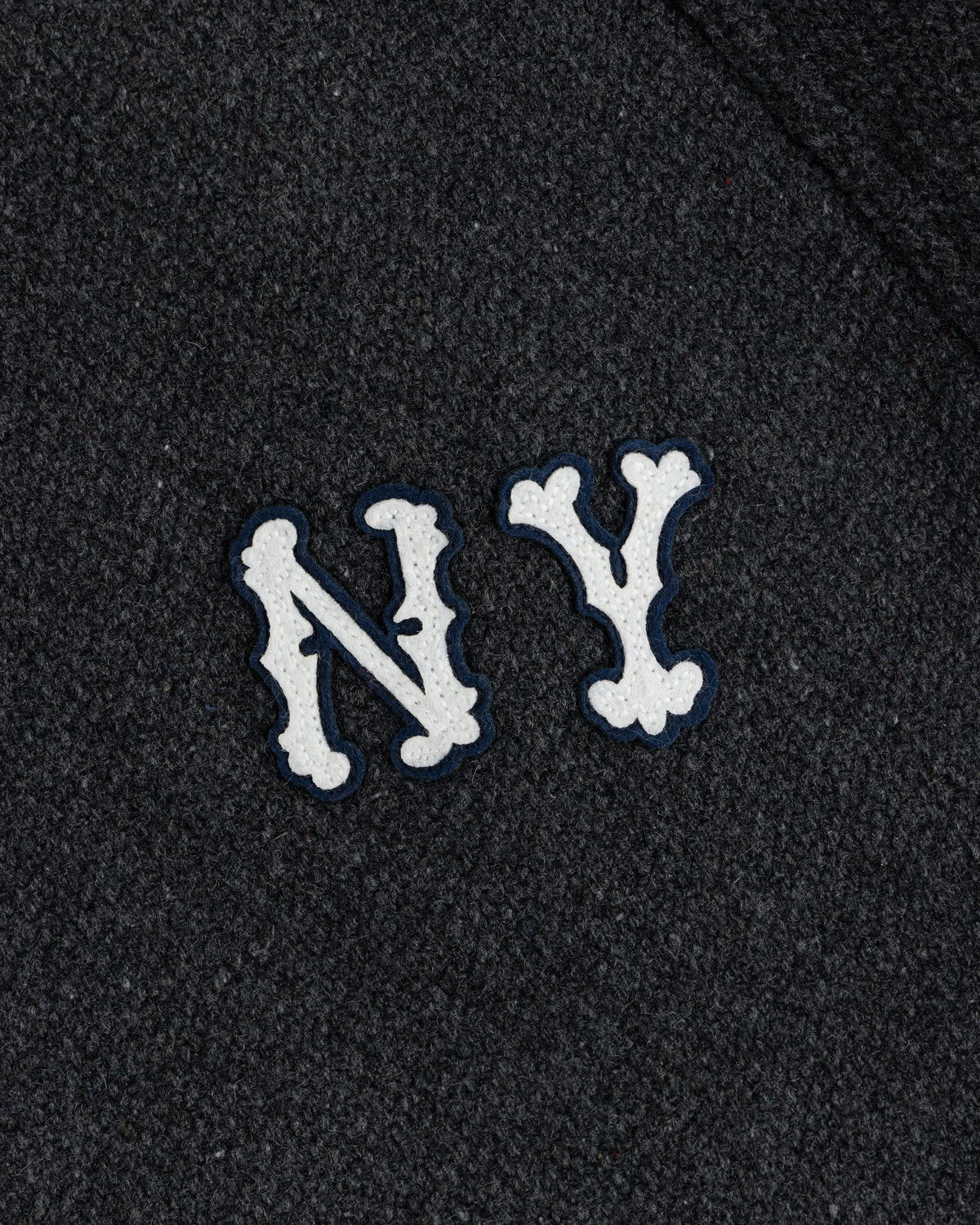 NY Highlanders Wool Varsity Jacket with white, bone-styled NY letters on dark textured fabric.