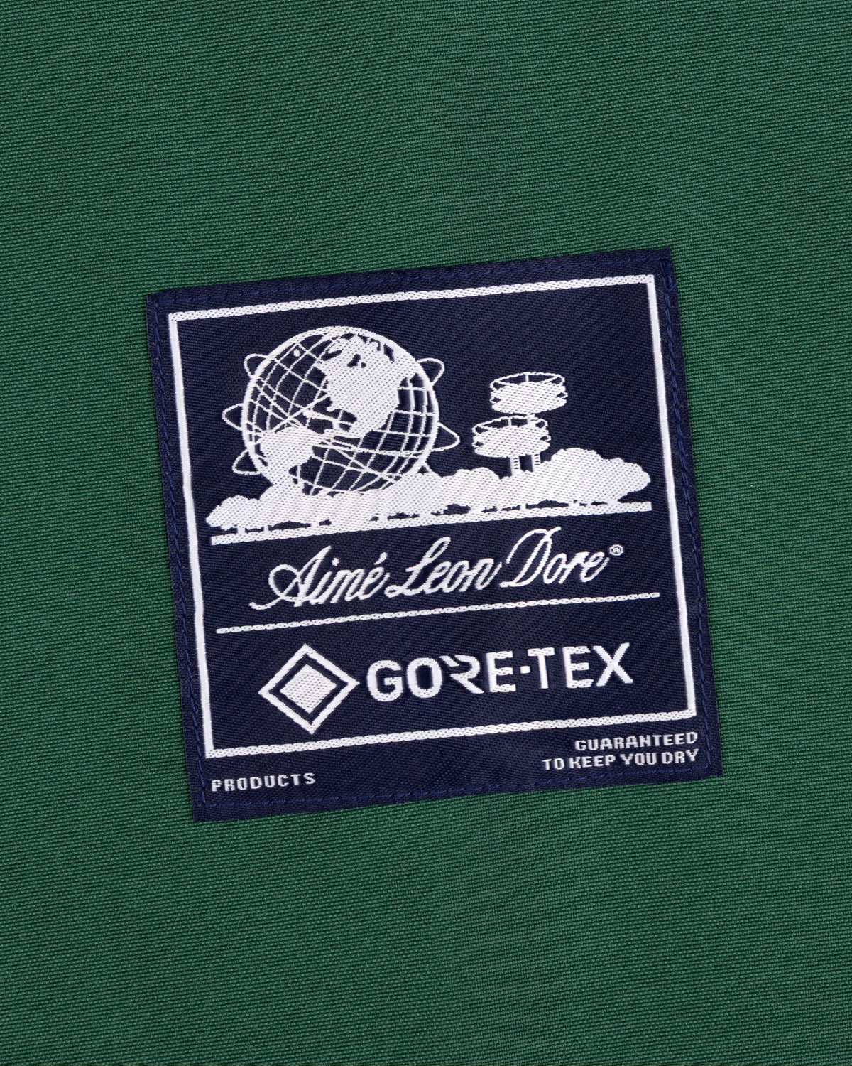 A navy GORE-TEX Striped Sailing Jacket by Aimé Leon Dore, with a logo patch showing a globe, clouds, and text.