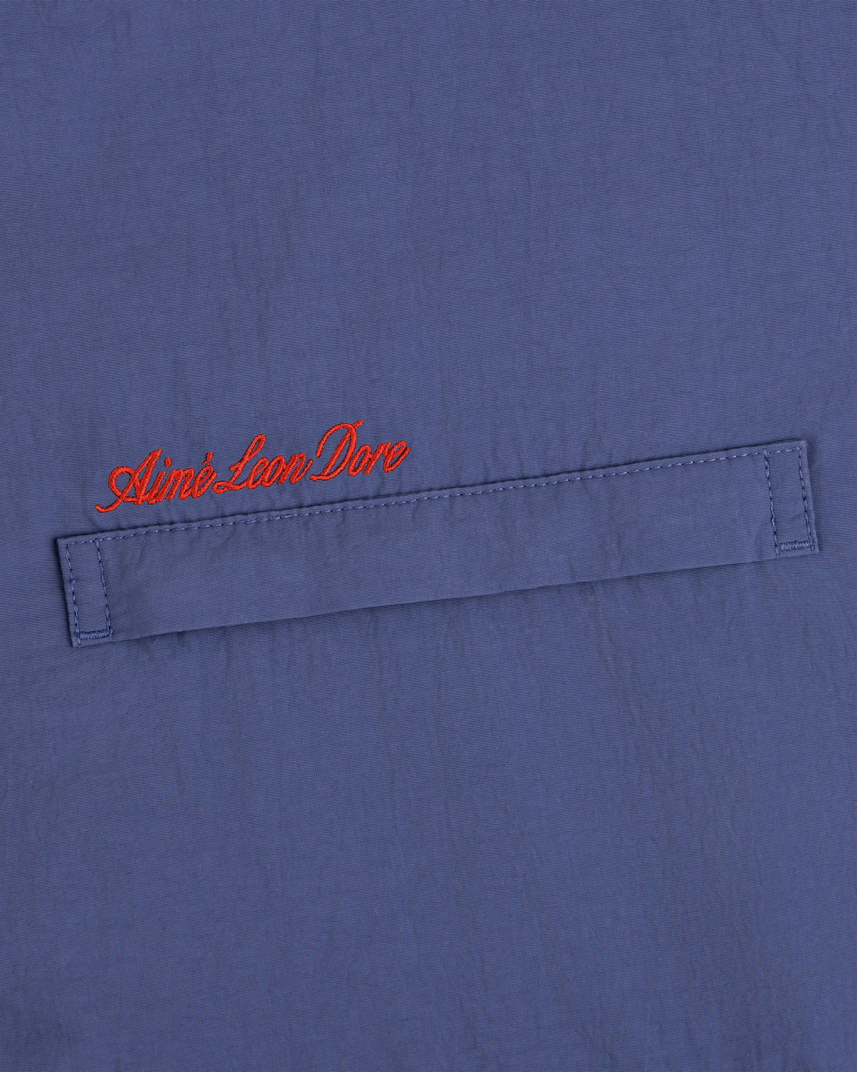 Blue Fleece Lined Sport Windbreaker with a stitched flap and Aimé Leon Dore embroidered in red cursive above.