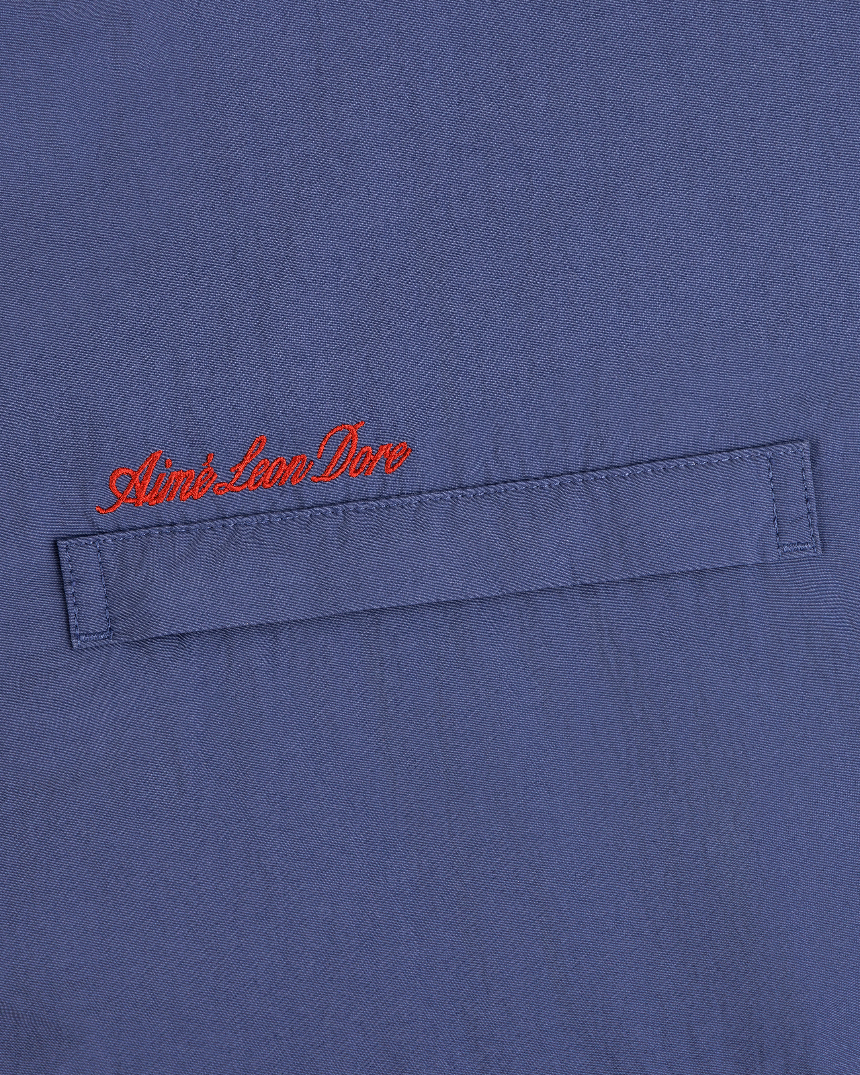 Blue Fleece Lined Sport Windbreaker with a stitched flap and Aimé Leon Dore embroidered in red cursive above.