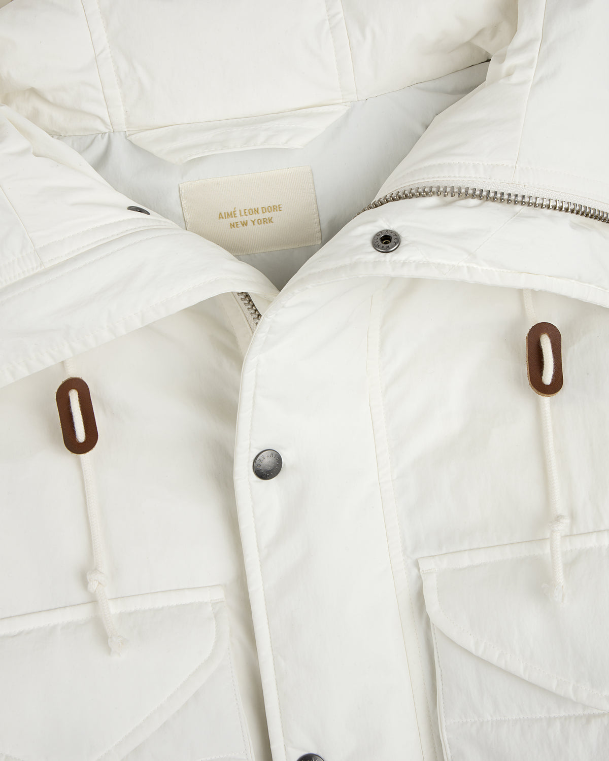 Close-up of a white Down-Filled Surplus Parka with a metal zipper, snap buttons, and two brown drawstring toggles.