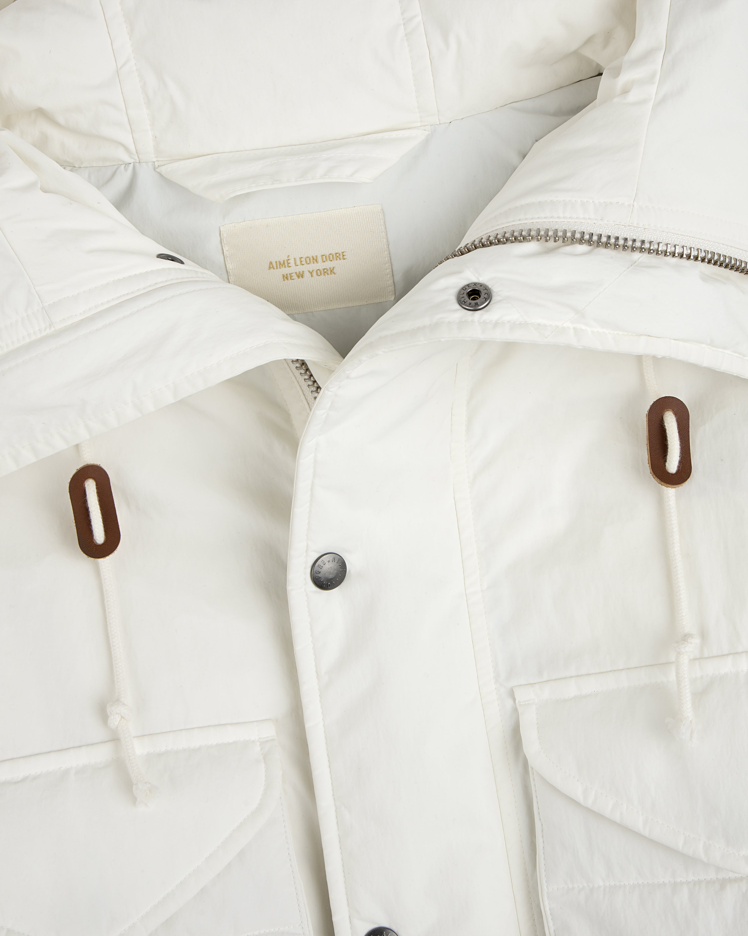 Close-up of a white Down-Filled Surplus Parka with a metal zipper, snap buttons, and two brown drawstring toggles.