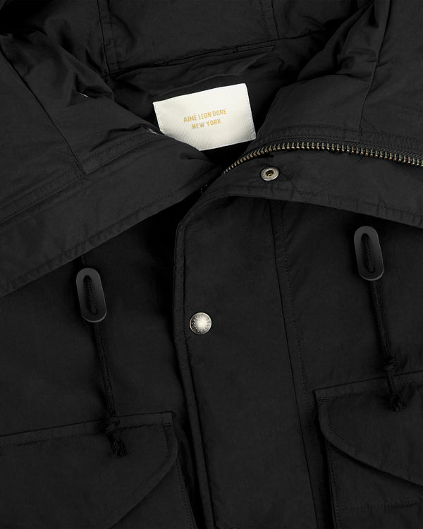 Close-up of a black Down-Filled Surplus Parka with a high collar, snap buttons, and two pockets with drawstring toggles.