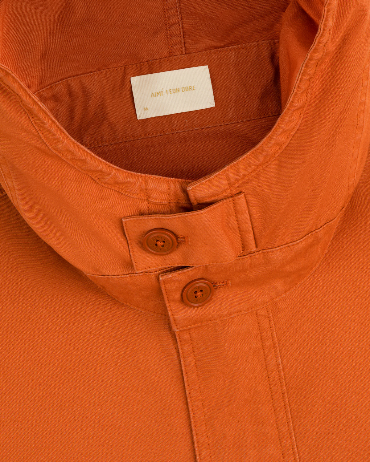 Close-up of a Garment Washed Anorak collar, featuring an orange button-front placket and an interior brand label.