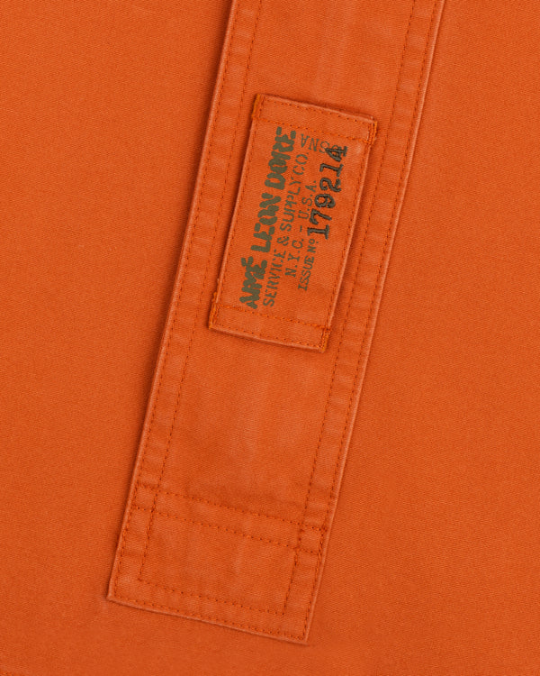 Orange Garment Washed Anorak fabric with a stitched rectangular patch featuring branded text and an issue number.