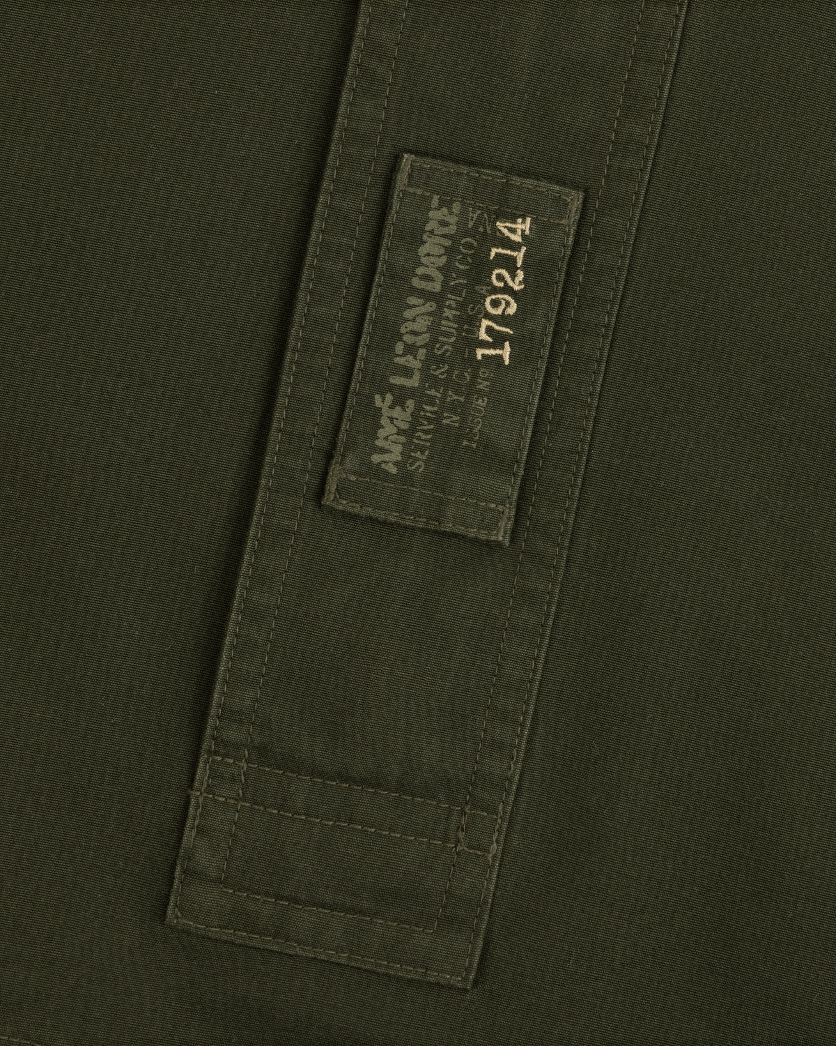Garment Washed Anorak in olive green with a rectangular patch featuring branded text and the number 179214.