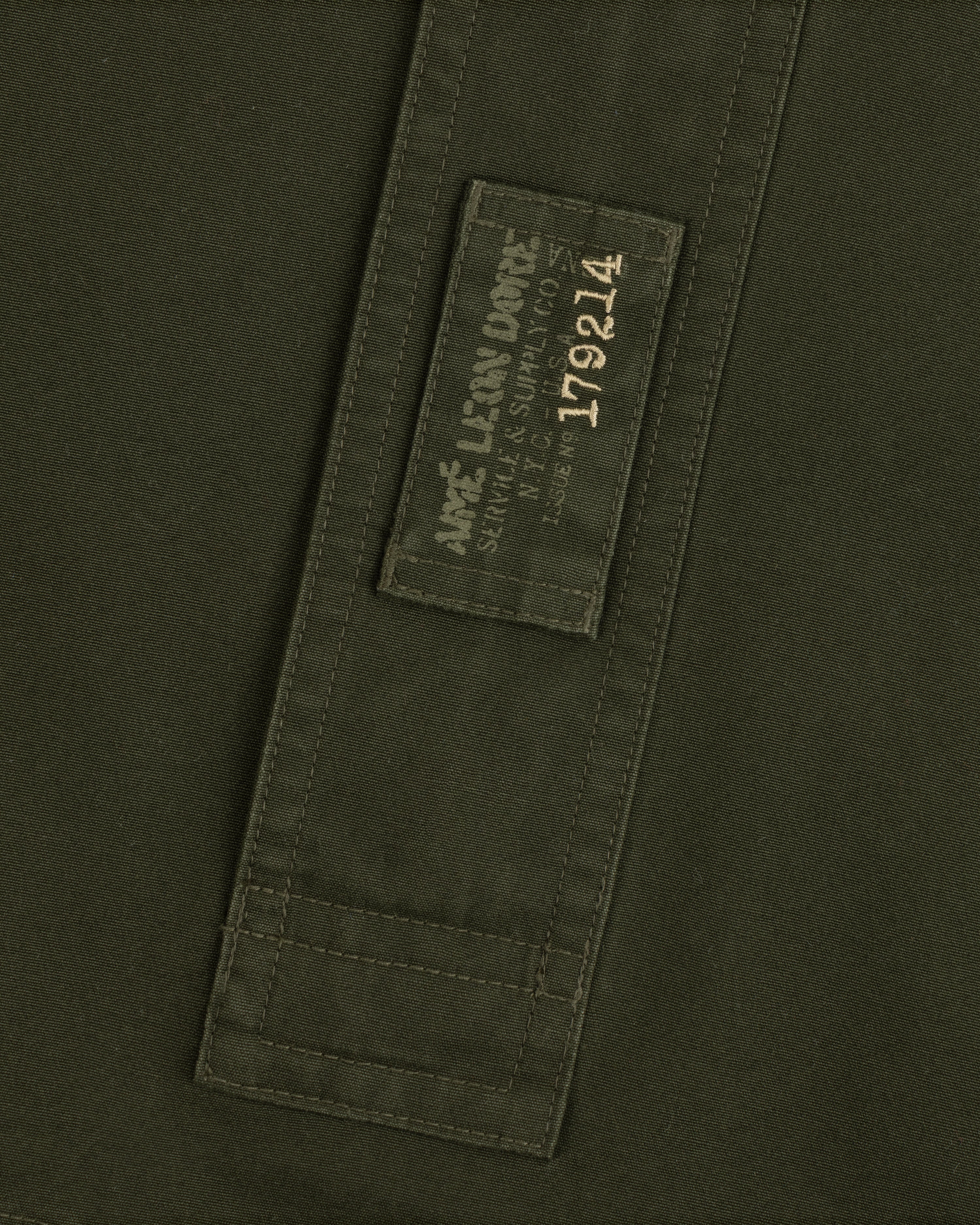 Garment Washed Anorak in olive green with a rectangular patch featuring branded text and the number 179214.