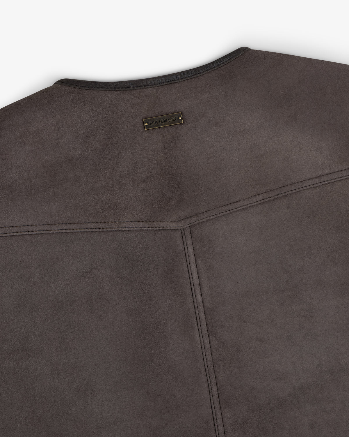 Back of a dark gray suede Shearling Biker Vest with a small, rectangular branded metal tag at the neckline.