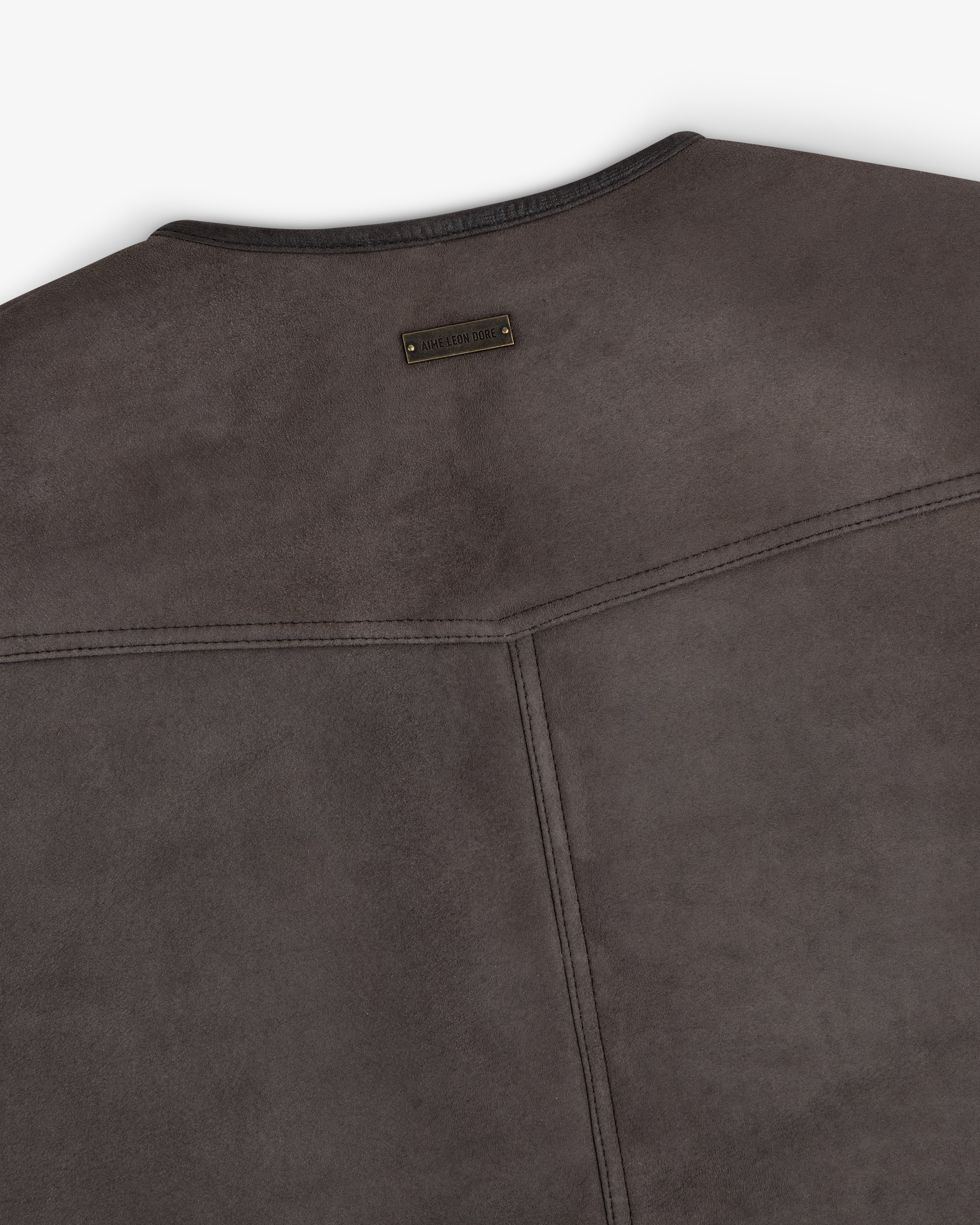 Back of a dark gray suede Shearling Biker Vest with a small, rectangular branded metal tag at the neckline.