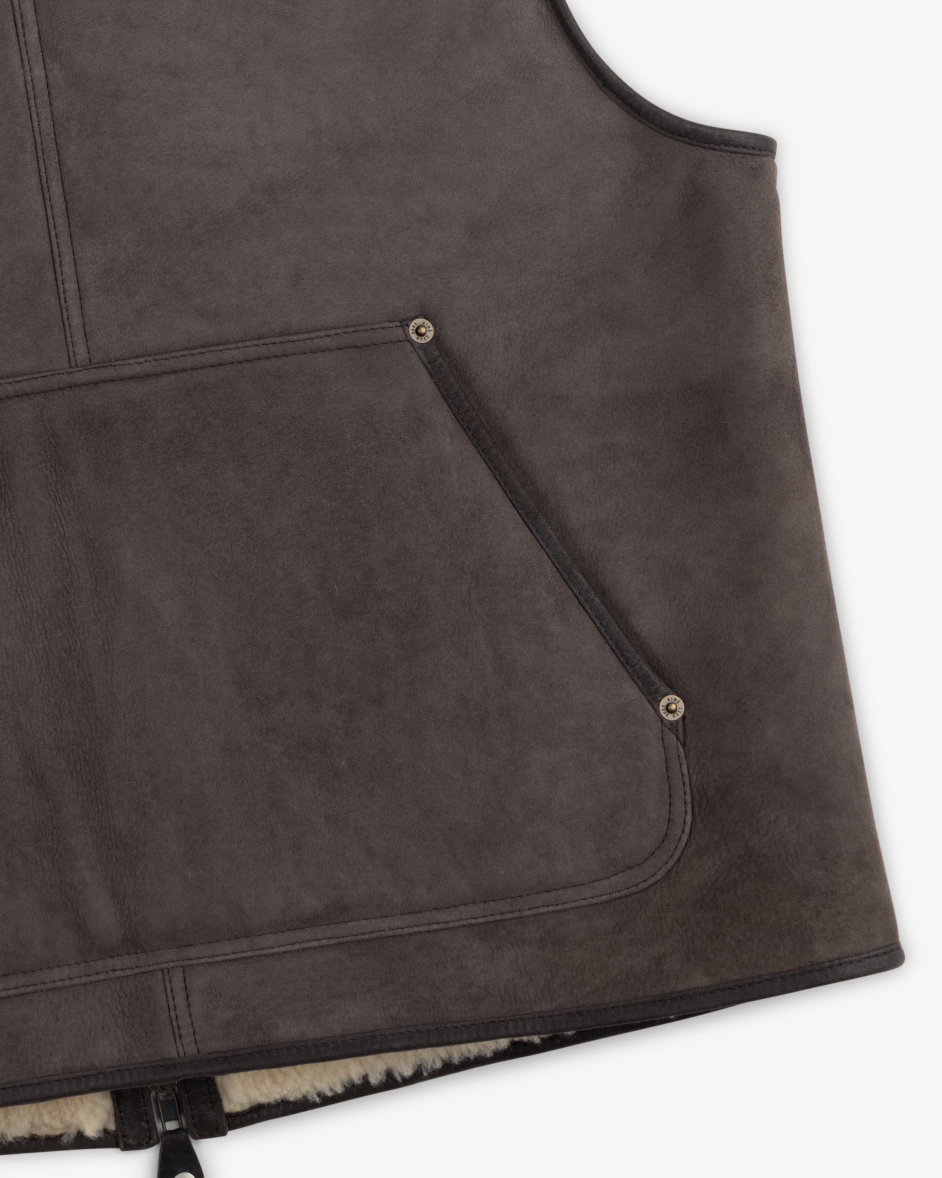 Close-up of a charcoal grey Shearling Biker Vest with a large front pocket reinforced with metal rivets.