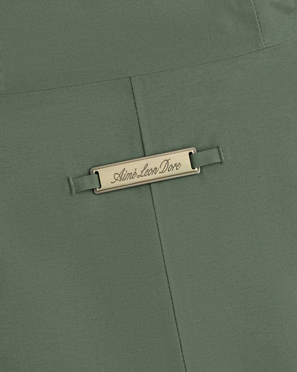 Olive green fabric of a GORE-TEX Down Filled Fishtail Parka with a rectangular metal plaque engraved Aimé Leon Dore.