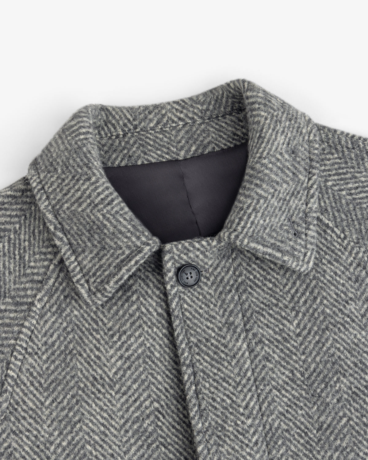 Close-up of a grey Wool Herringbone Overcoat featuring a pointed collar and a single front button.
