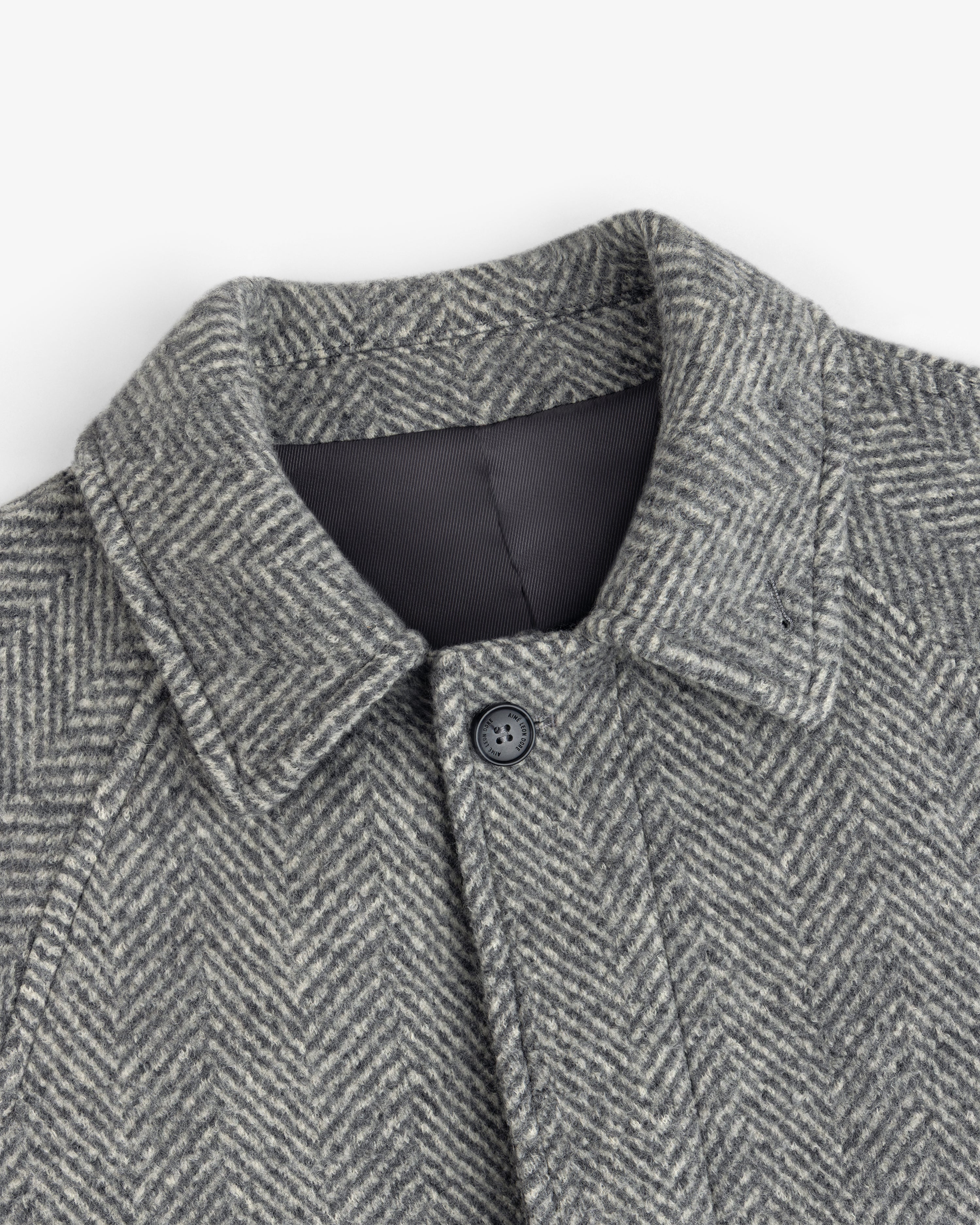 Close-up of a grey Wool Herringbone Overcoat featuring a pointed collar and a single front button.