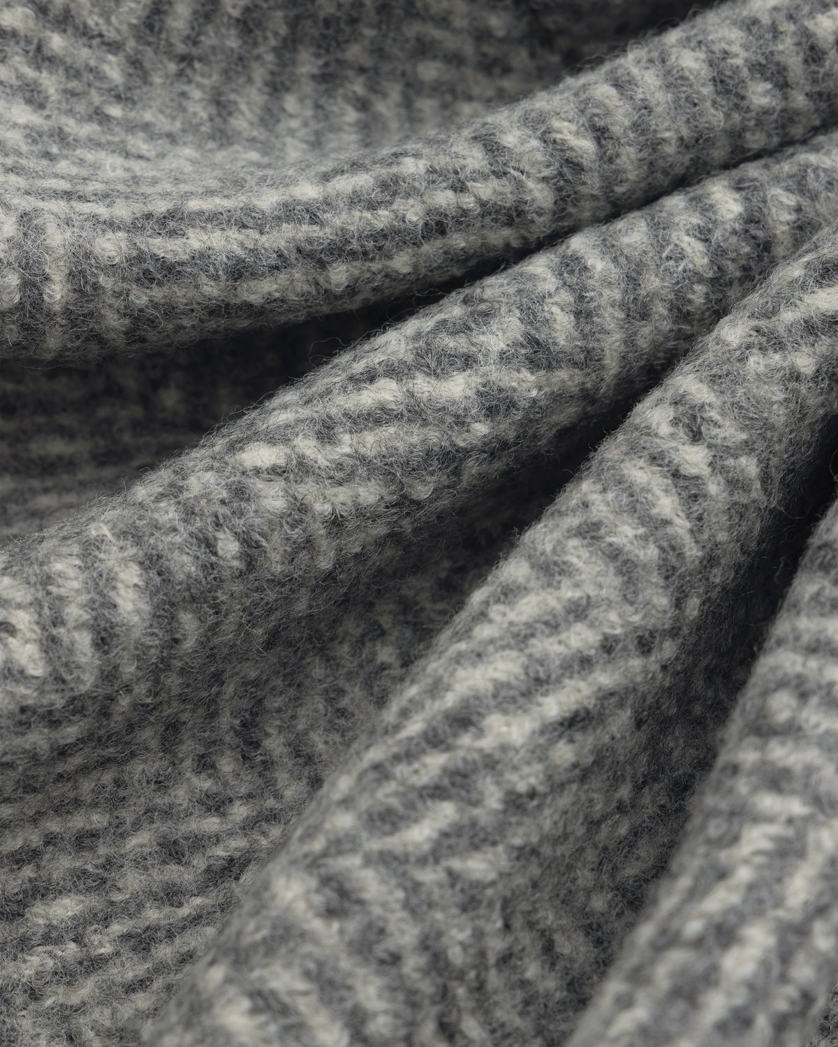 Close-up of a grey and white Wool Herringbone Overcoat in folded fabric.