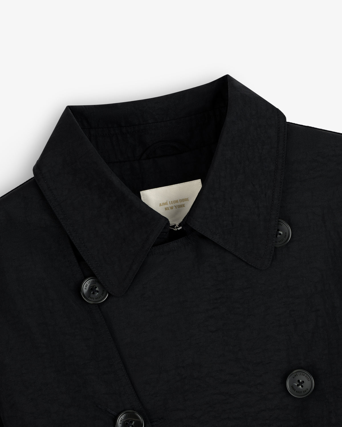 Close-up of a black Double Breasted Nylon Trench Coat with buttons and inner label, on a white background.