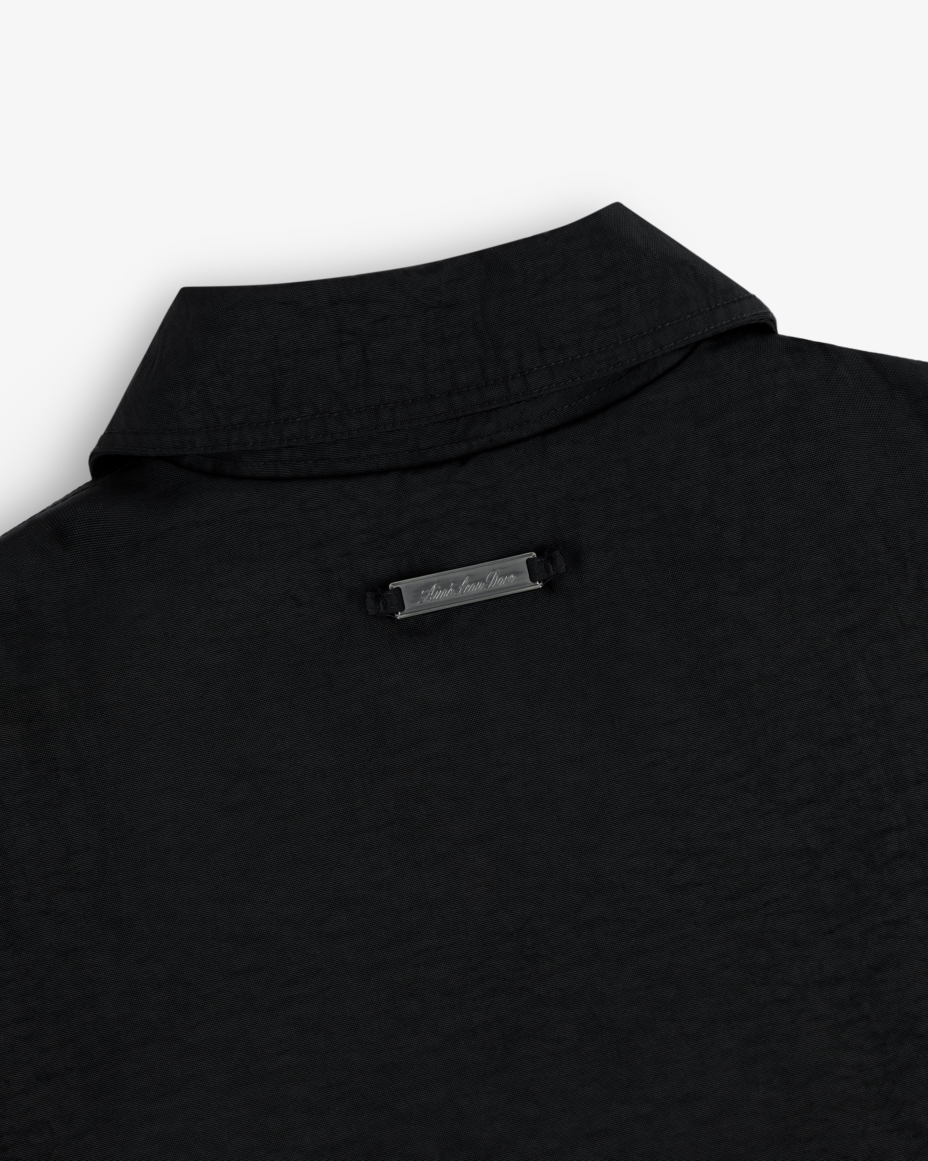 Close-up of the back collar of a nylon trench coat with a small metallic label below the collar.