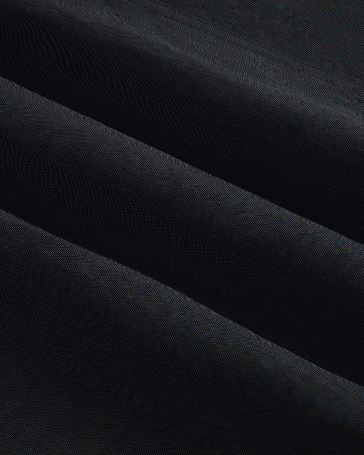 Close-up of Double Breasted Nylon Trench Coat fabric, showing its textured black material with subtle diagonal folds.