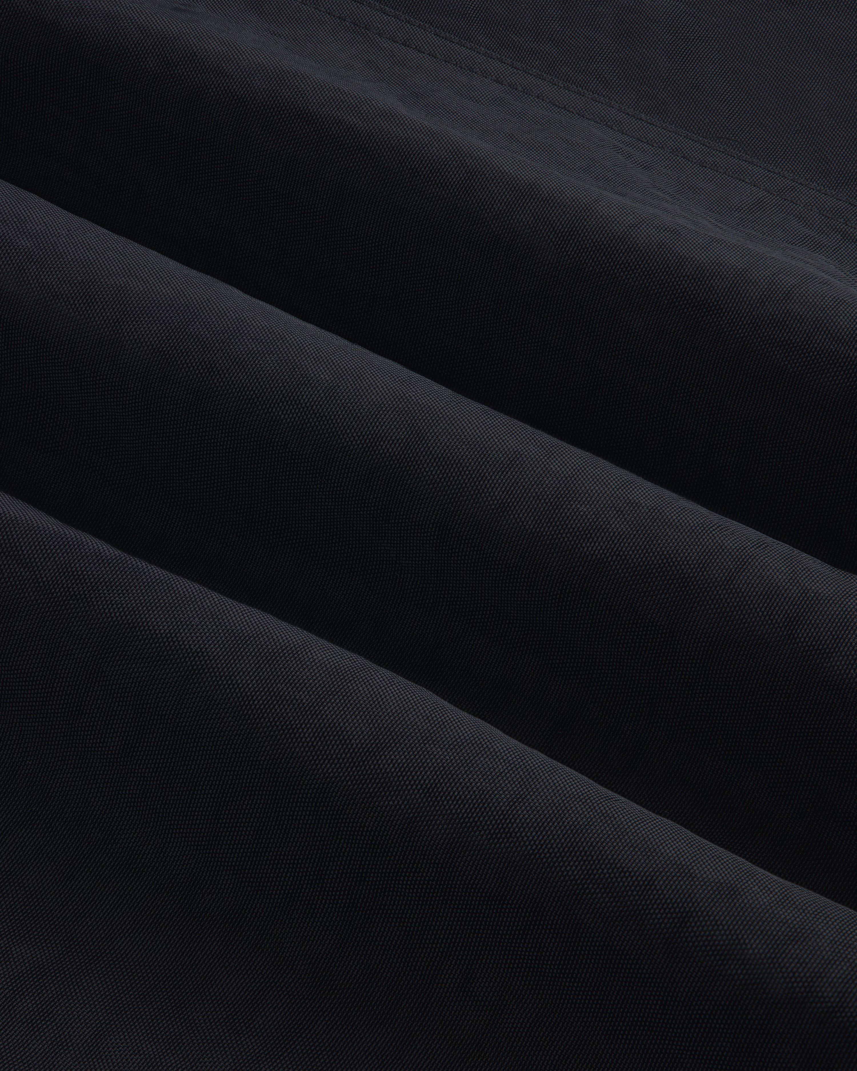 Close-up of Double Breasted Nylon Trench Coat fabric, showing its textured black material with subtle diagonal folds.
