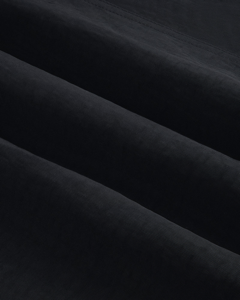 Close-up of Double Breasted Nylon Trench Coat fabric, showing its textured black material with subtle diagonal folds.