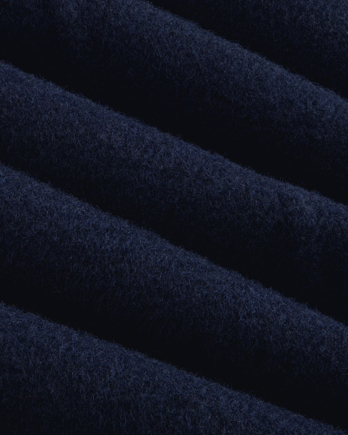 Close-up of navy blue wool fabric with diagonal folds on a Reversible Double Breasted Top Coat.