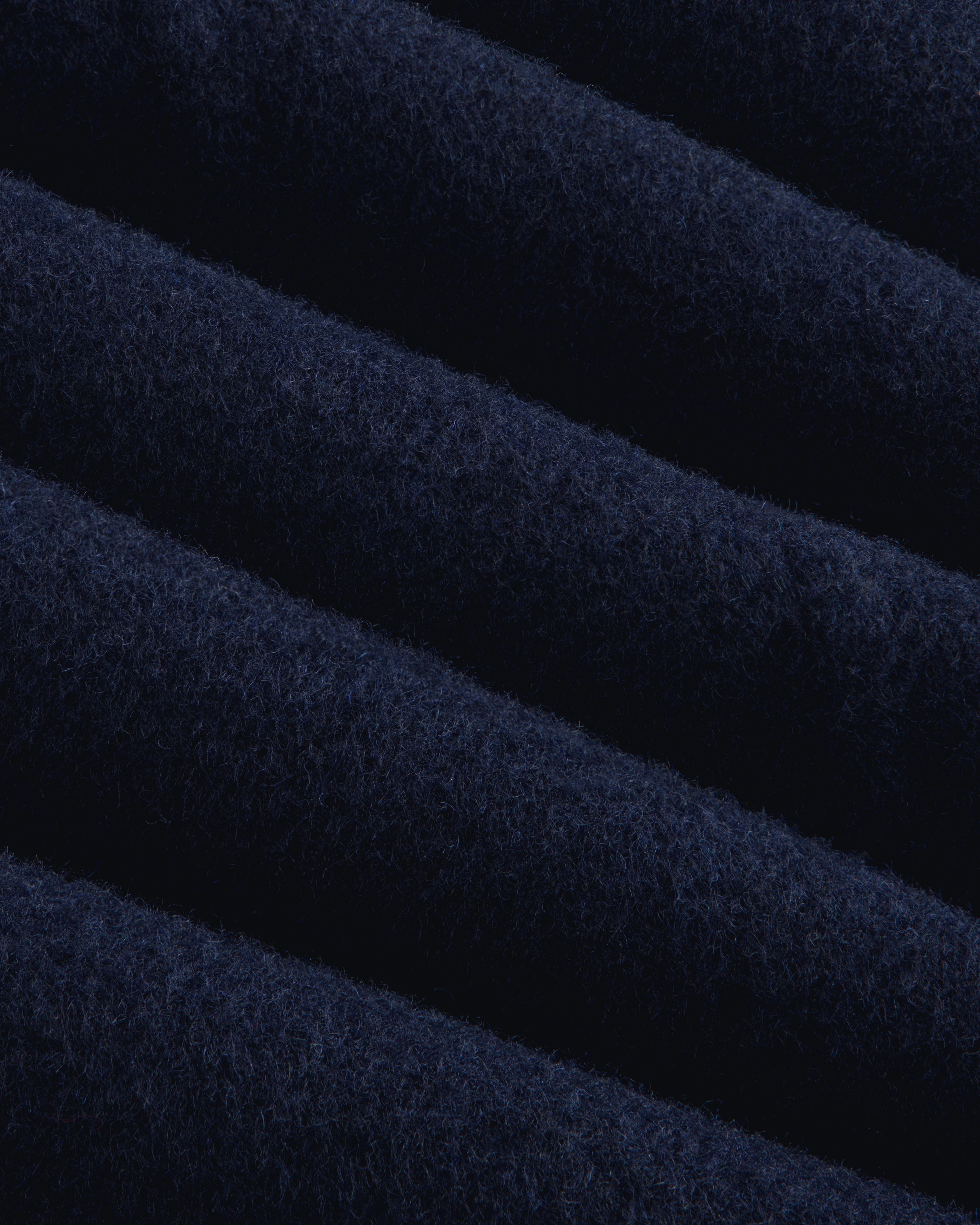 Close-up of navy blue wool fabric with diagonal folds on a Reversible Double Breasted Top Coat.